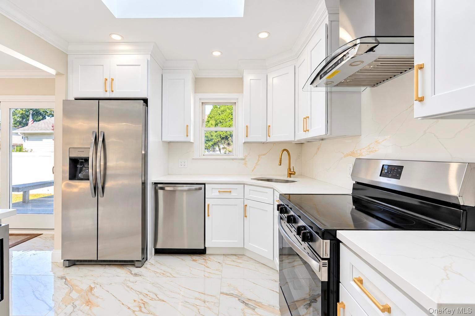 Kitchen featuring white shaker-style cabinetry, gold-tone hardware, stainless steel appliances, white stone-finish countertops with matching backsplas