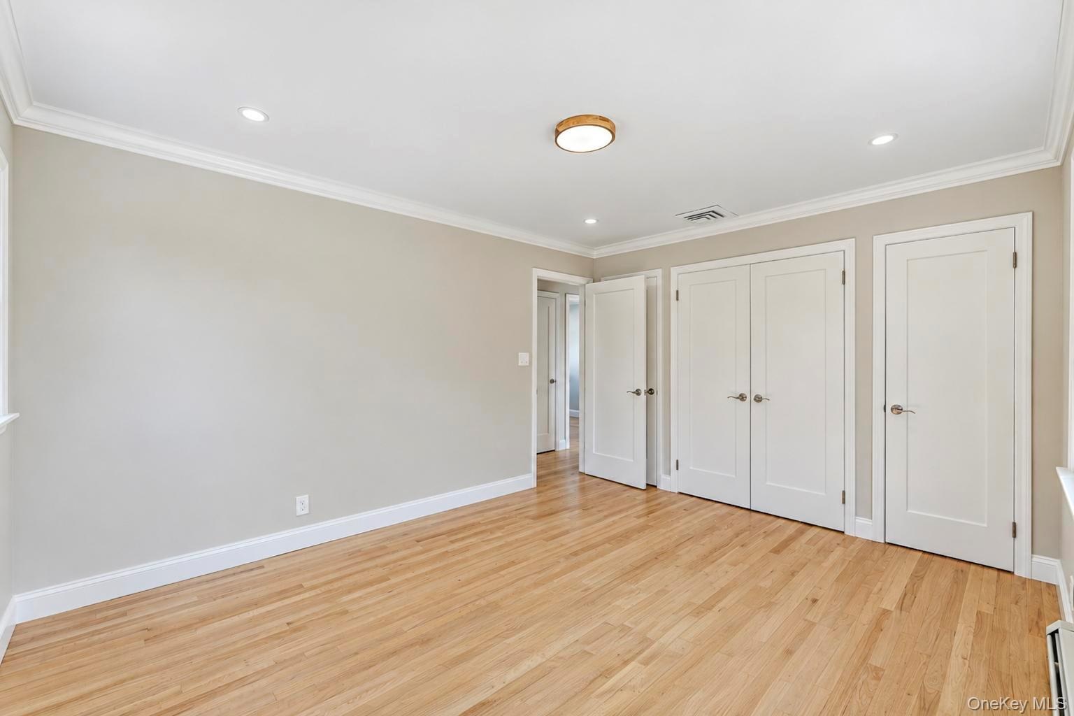 Room featuring light wood-finish flooring, neutral wall paint, recessed lighting, crown molding, and white solid-core interior doors with satin nickel