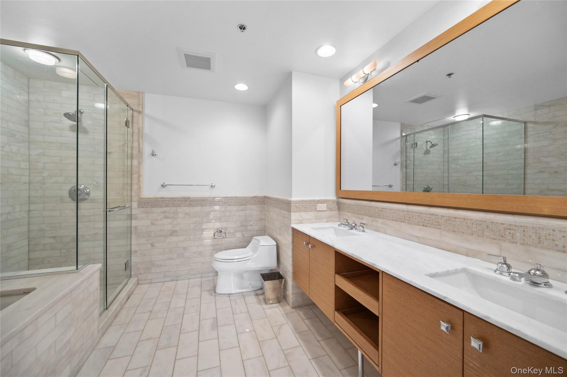 Bathroom featuring tile walls, double vanity, a stall shower, toilet, and a bathtub