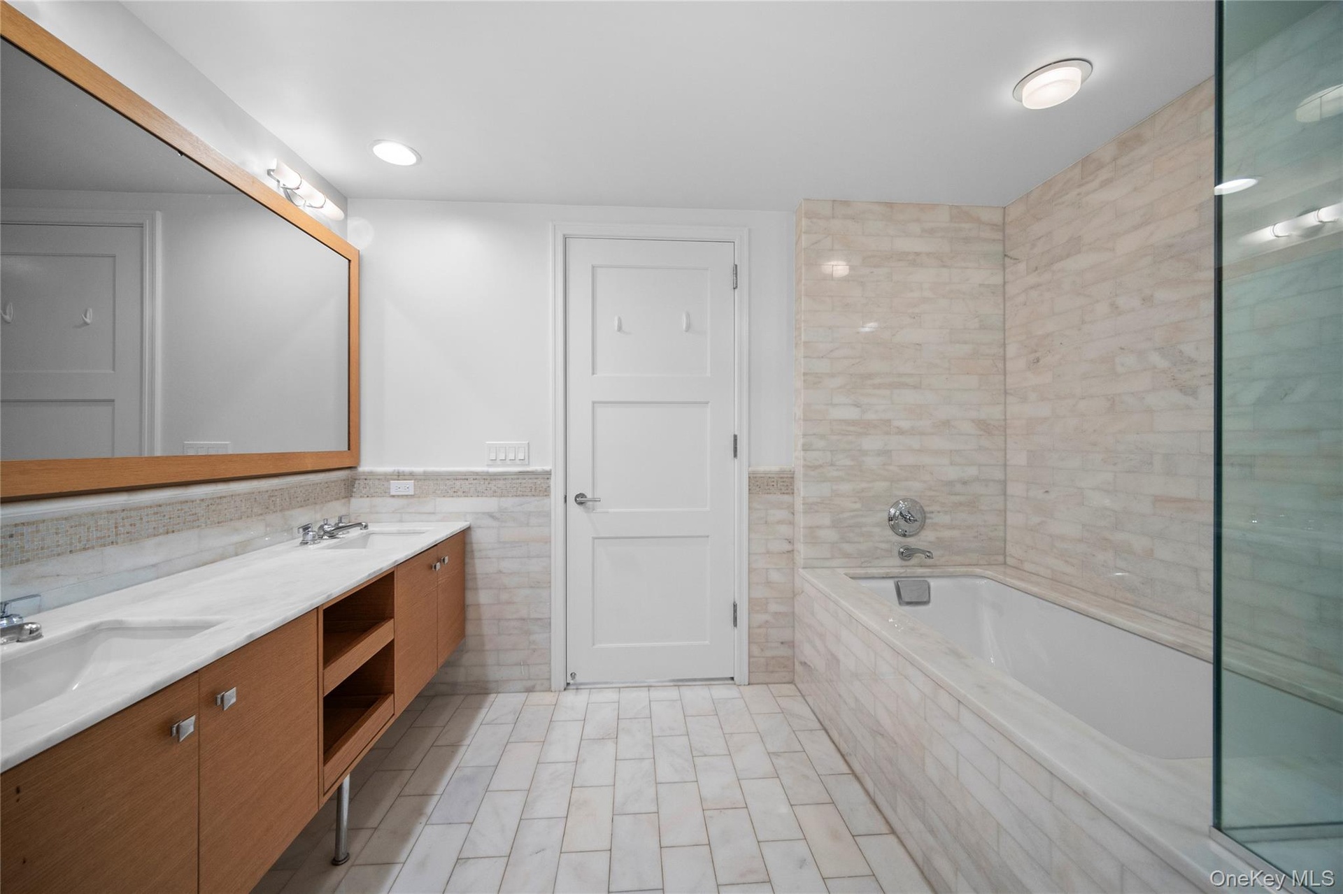 Bathroom featuring tile walls, double vanity, a garden tub, and a wainscoted wall