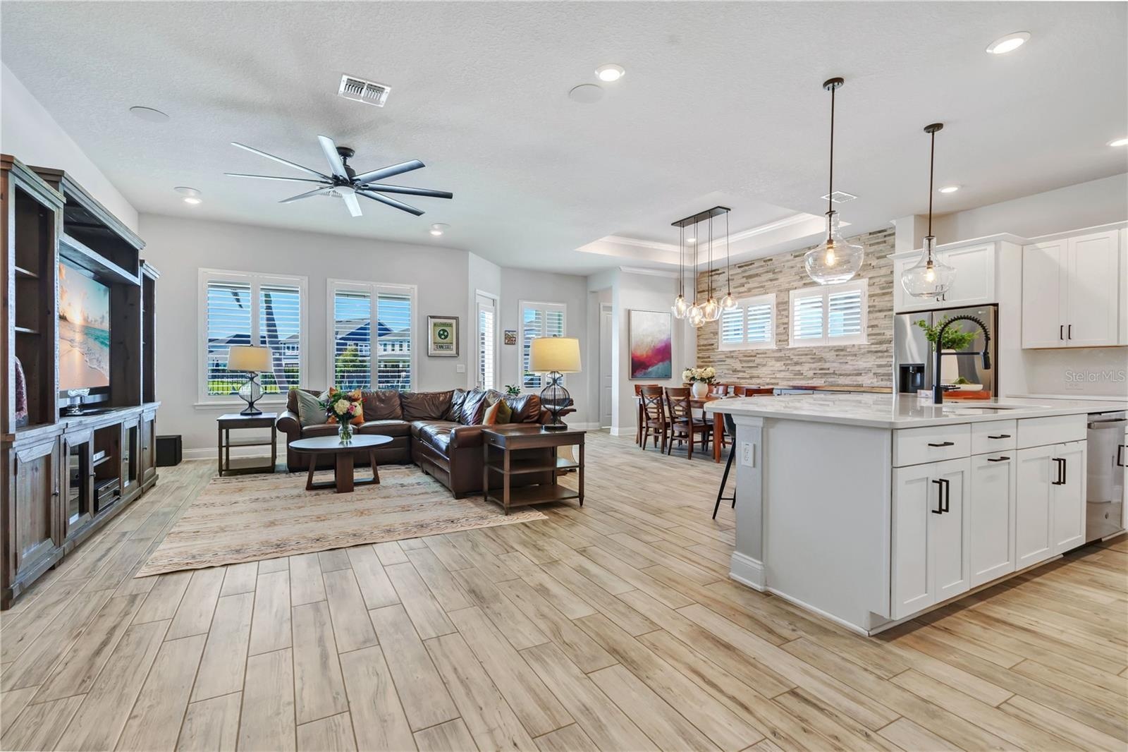 Open floor plan connecting the great room, kitchen, and dining area. Wood look plank tile, crown moulding, and natural light throughout this one story