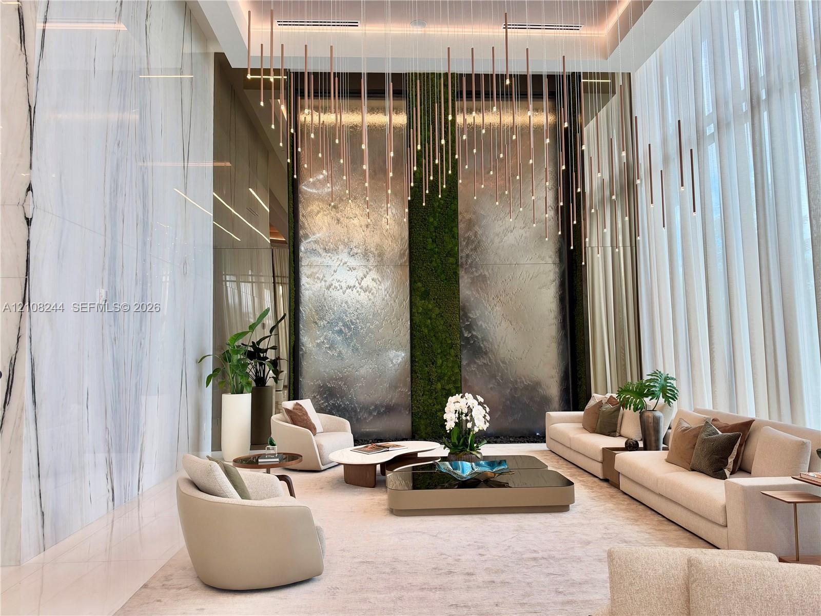 Double-height ceiling, large-scale veined stone wall cladding, floor-to-ceiling windows, custom tiered pendant lighting, and a floor-to-ceiling illumi
