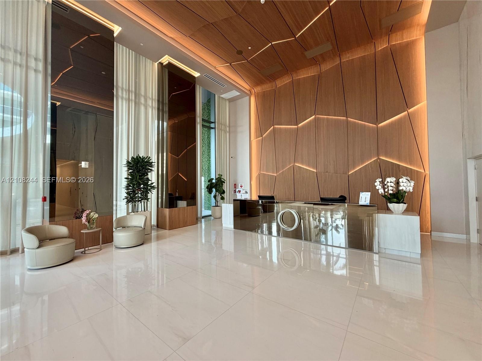 Lobby featuring high-gloss tile flooring, floor-to-ceiling windows with full-length drapery, geometric wood-paneled walls with integrated accent light