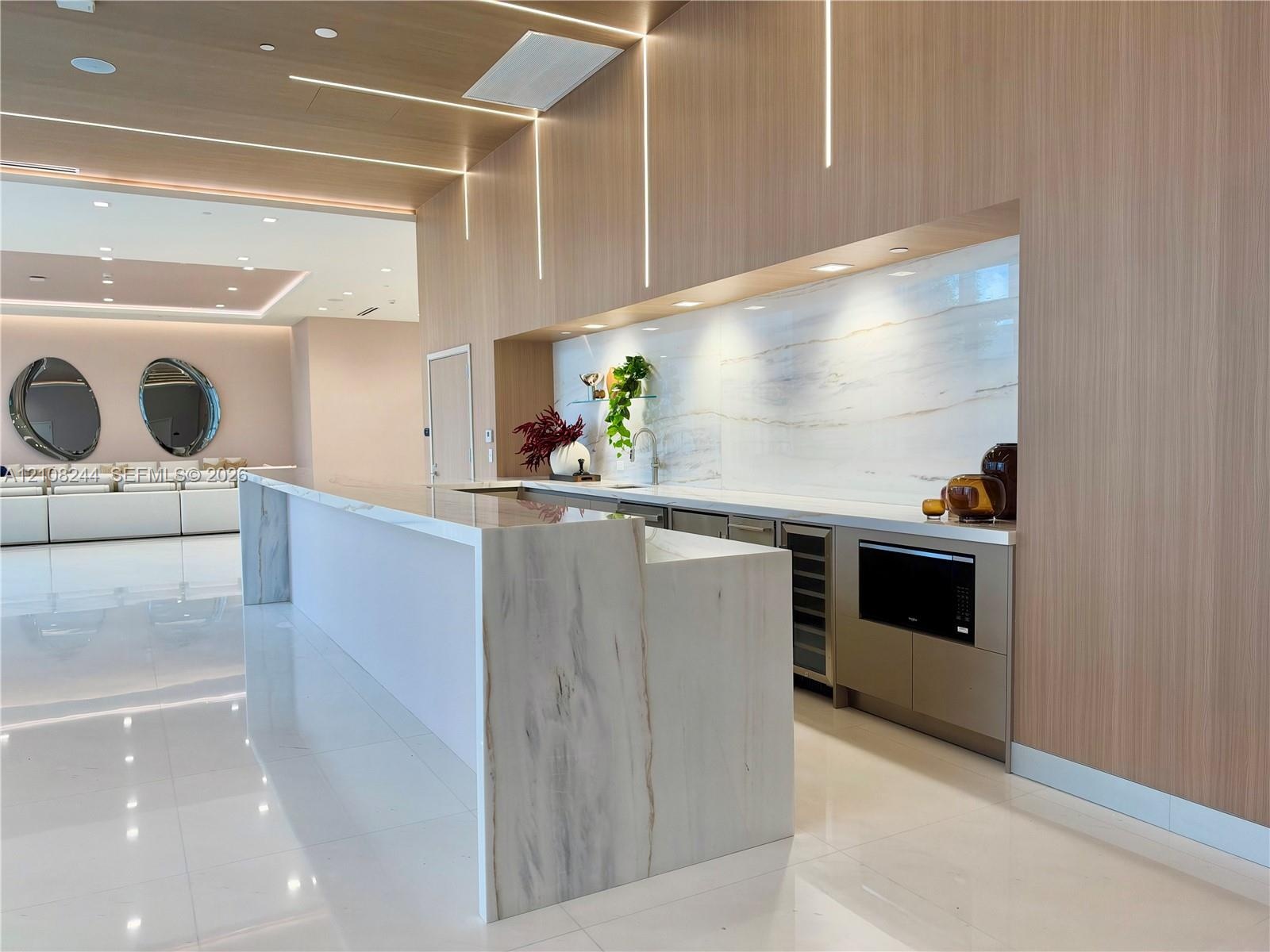 Custom kitchen area featuring stone slab countertops, waterfall-edge island, integrated cabinetry, light-toned wood paneling, and vertical recessed li