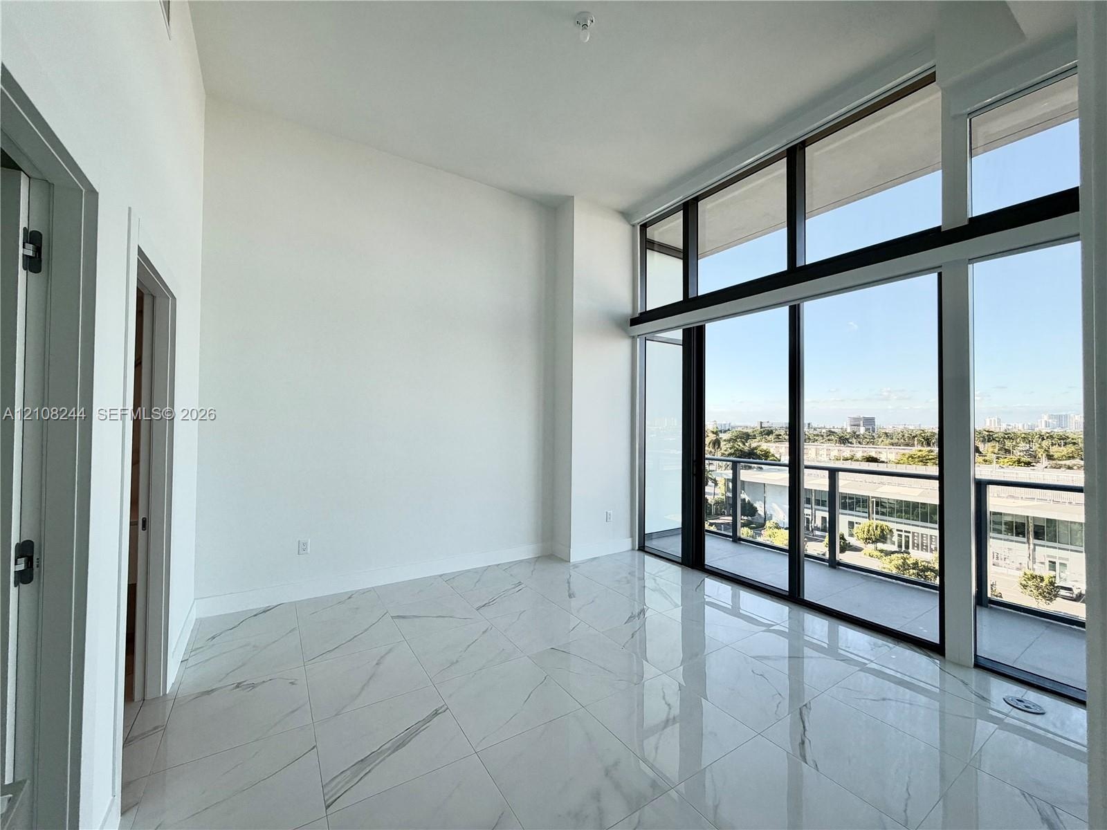 High-ceiling living area featuring large-format polished stone-finish flooring, floor-to-ceiling windows with dark framing, and a private balcony