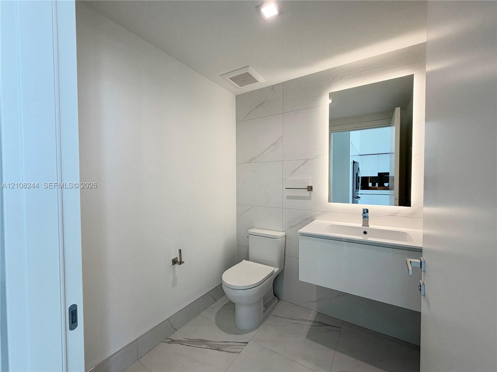 Contemporary bathroom featuring a floating white vanity, polished large-format tile flooring, wall-to-wall decorative tile backsplash, and a modern ba