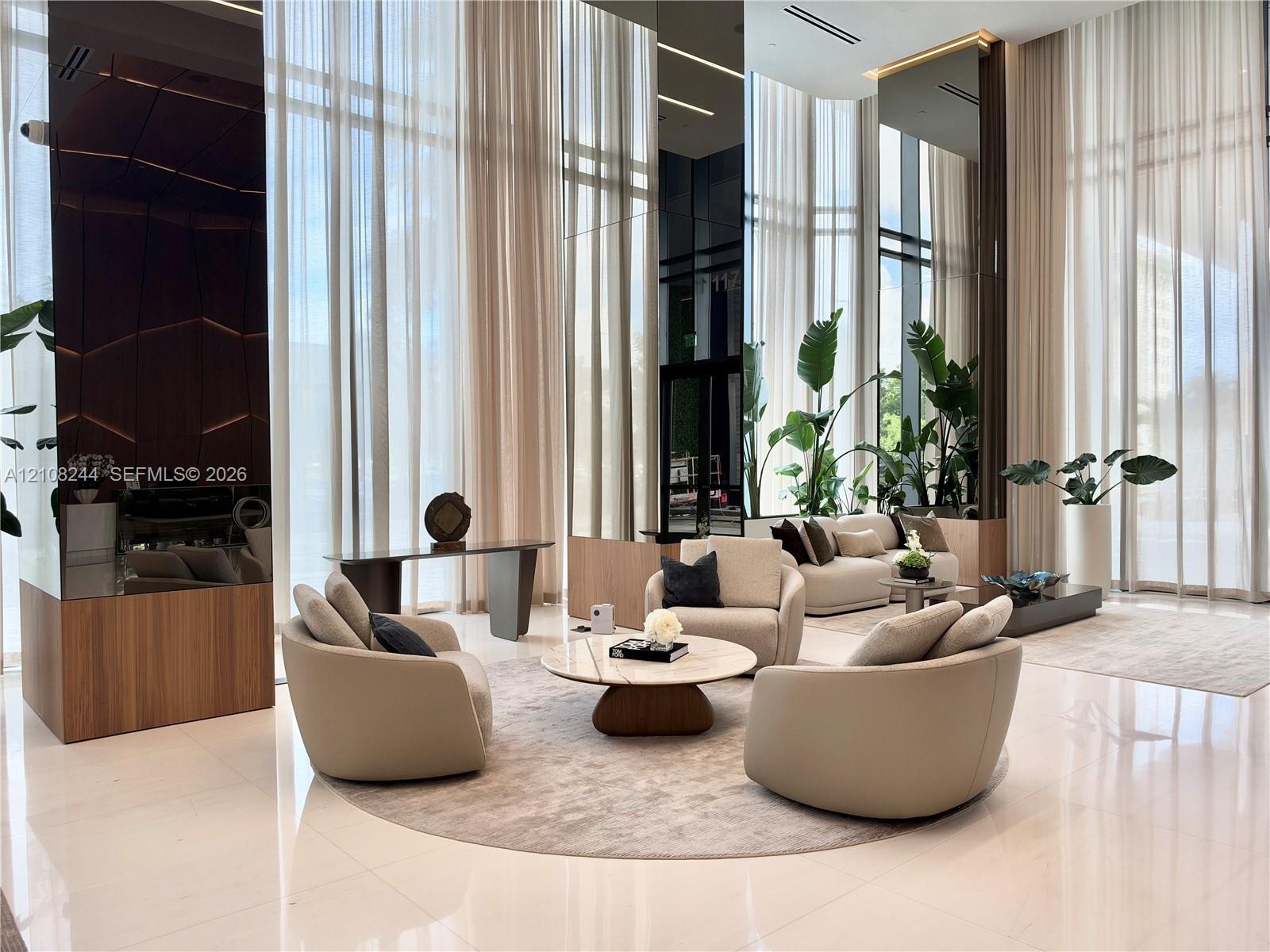 Double-height ceilings featuring floor-to-ceiling glass windows, polished stone flooring, and mirrored architectural columns