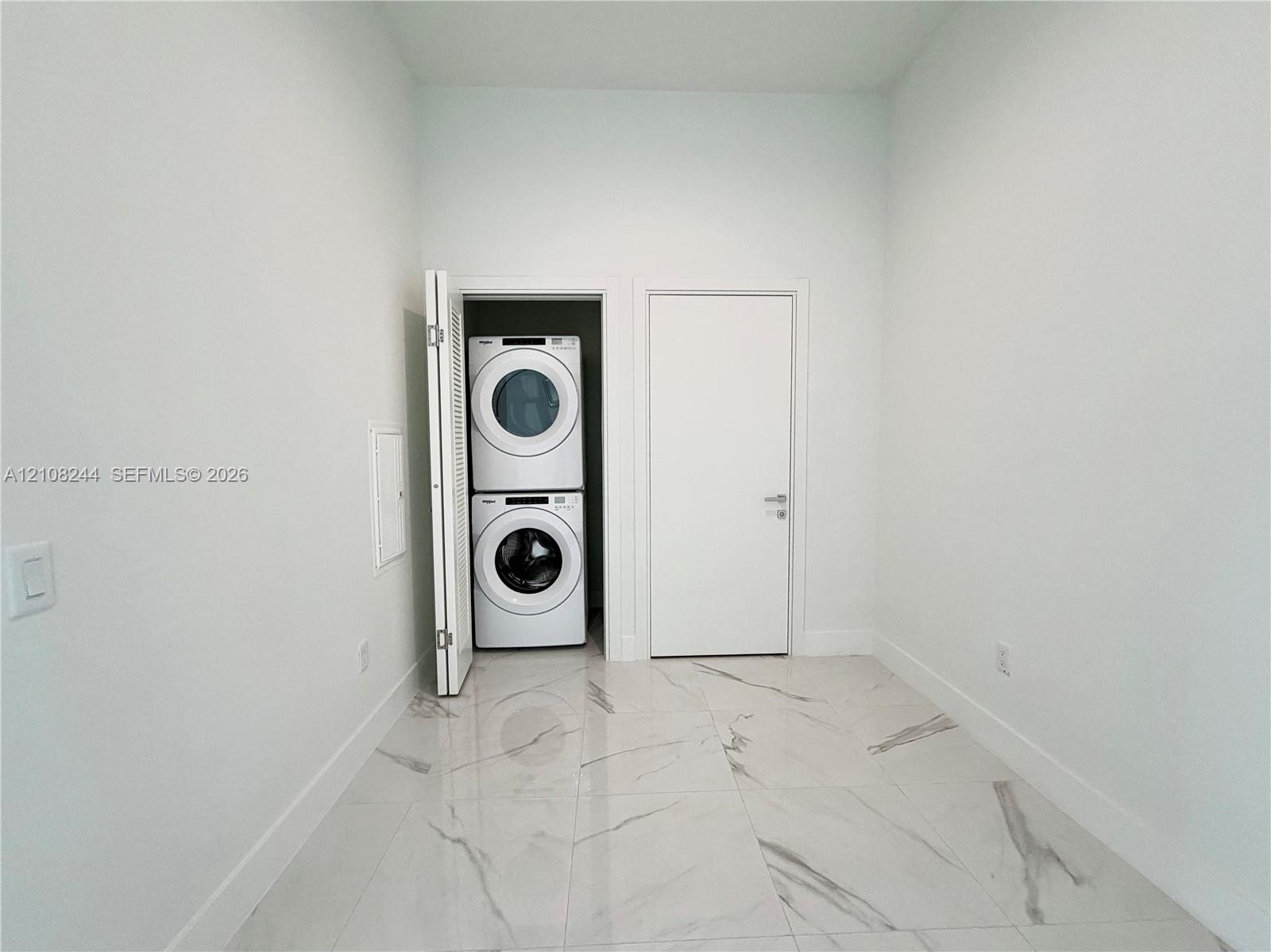 Dedicated utility space featuring stone-finish floor tile, a recessed laundry closet, and a stackable washer and dryer unit