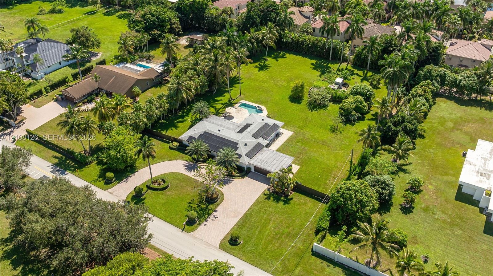 Aerial perspective of an expansive lot featuring a multi-gabled residence, a paved circular driveway, a private in-ground swimming pool, and solar pan