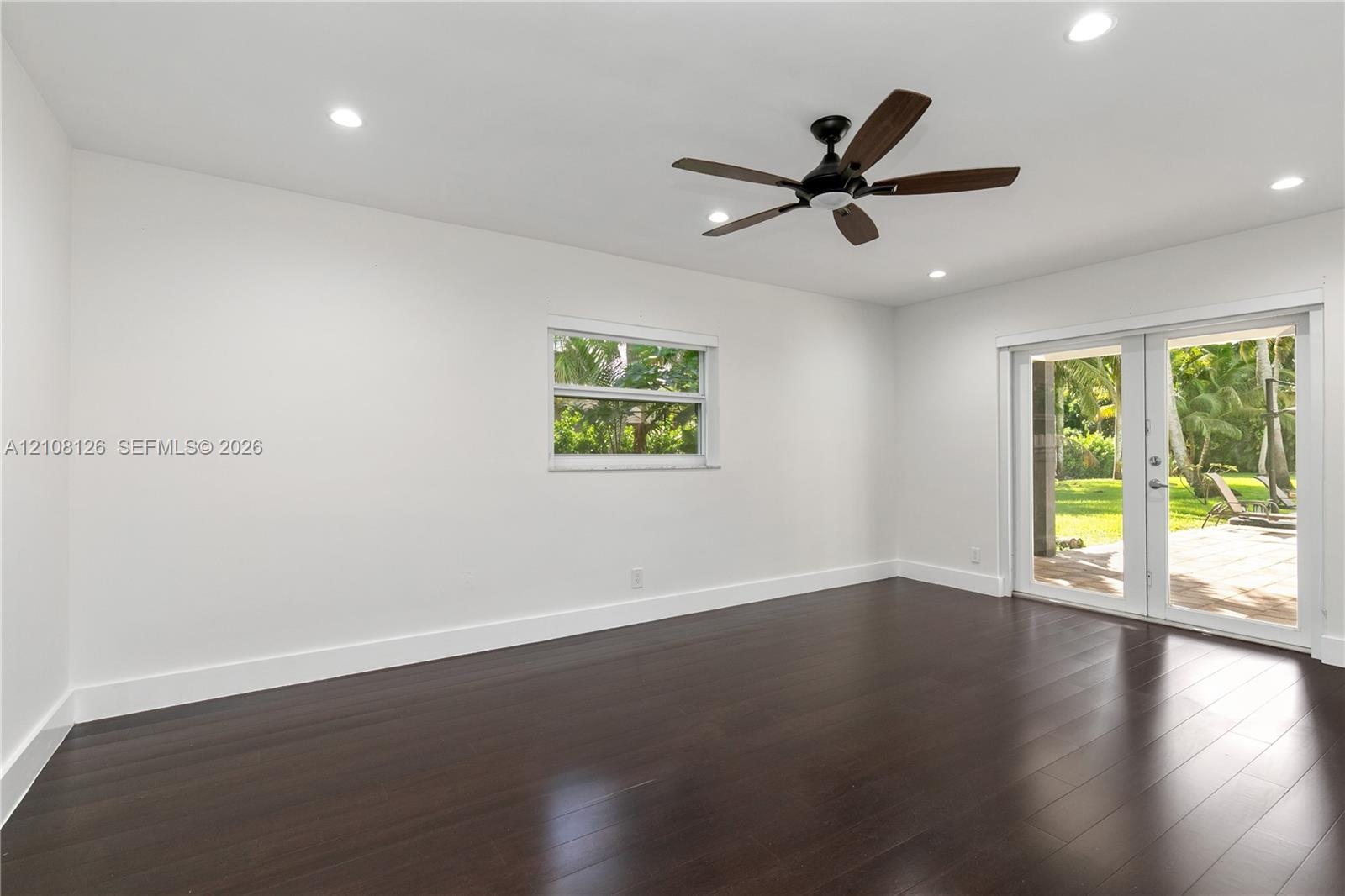 Dark wood-finish flooring, recessed lighting, ceiling fan, single-hung window, and glass-paned double doors