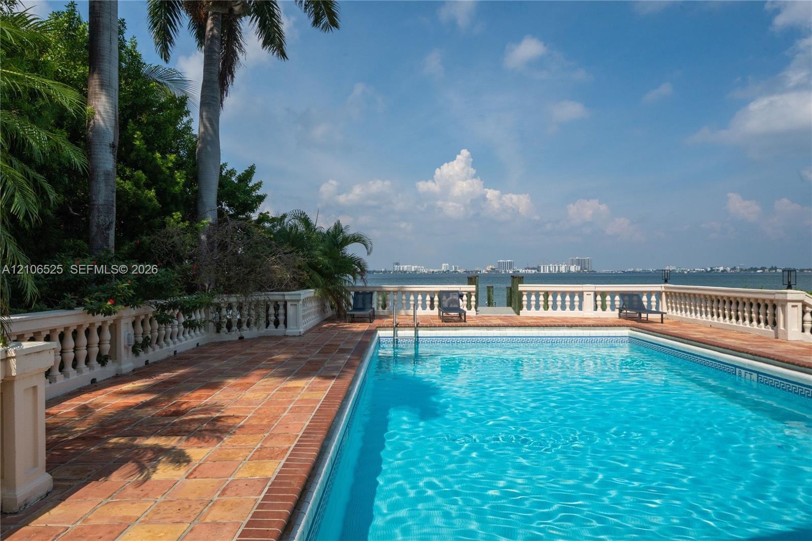 Swimming pool with tile surround, terracotta paver decking, decorative stone balustrade, and direct waterfront access