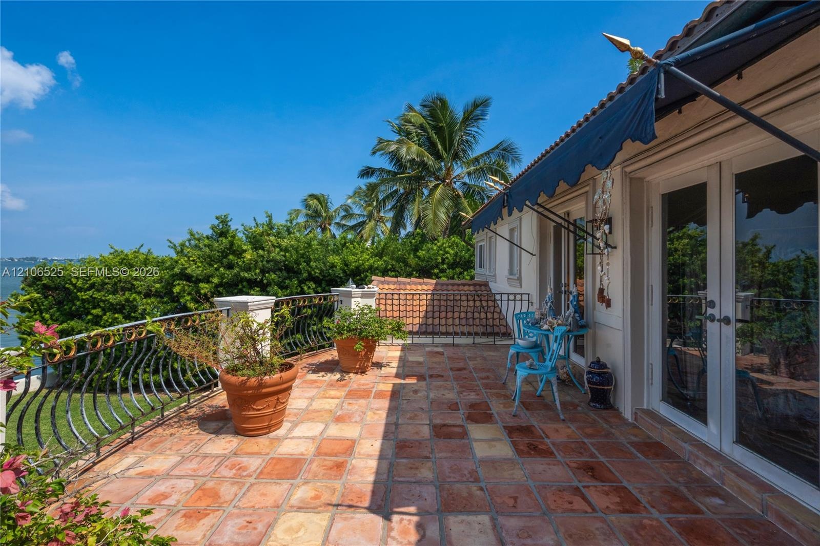 Terrace featuring terracotta tile flooring, wrought-iron railings, a retractable fabric awning, and dual-pane glass doors