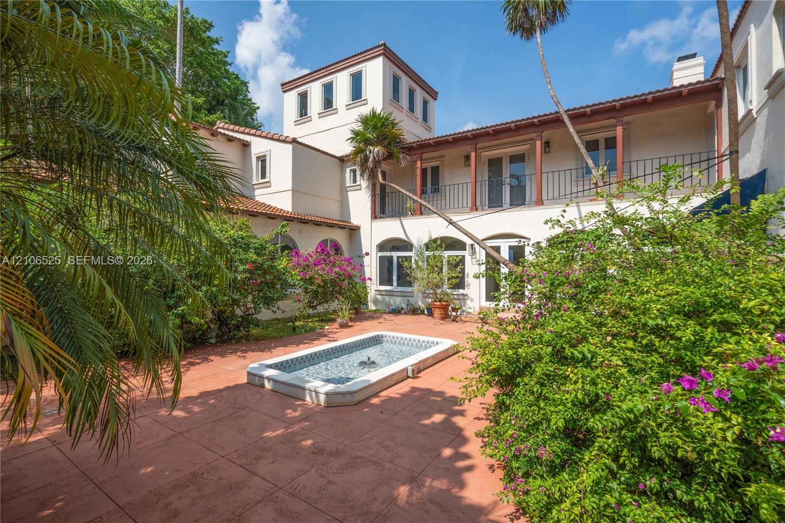 Courtyard featuring terra-cotta tile paving, a recessed water feature with decorative tile inlay, a second-story balcony with metal railing, and arche