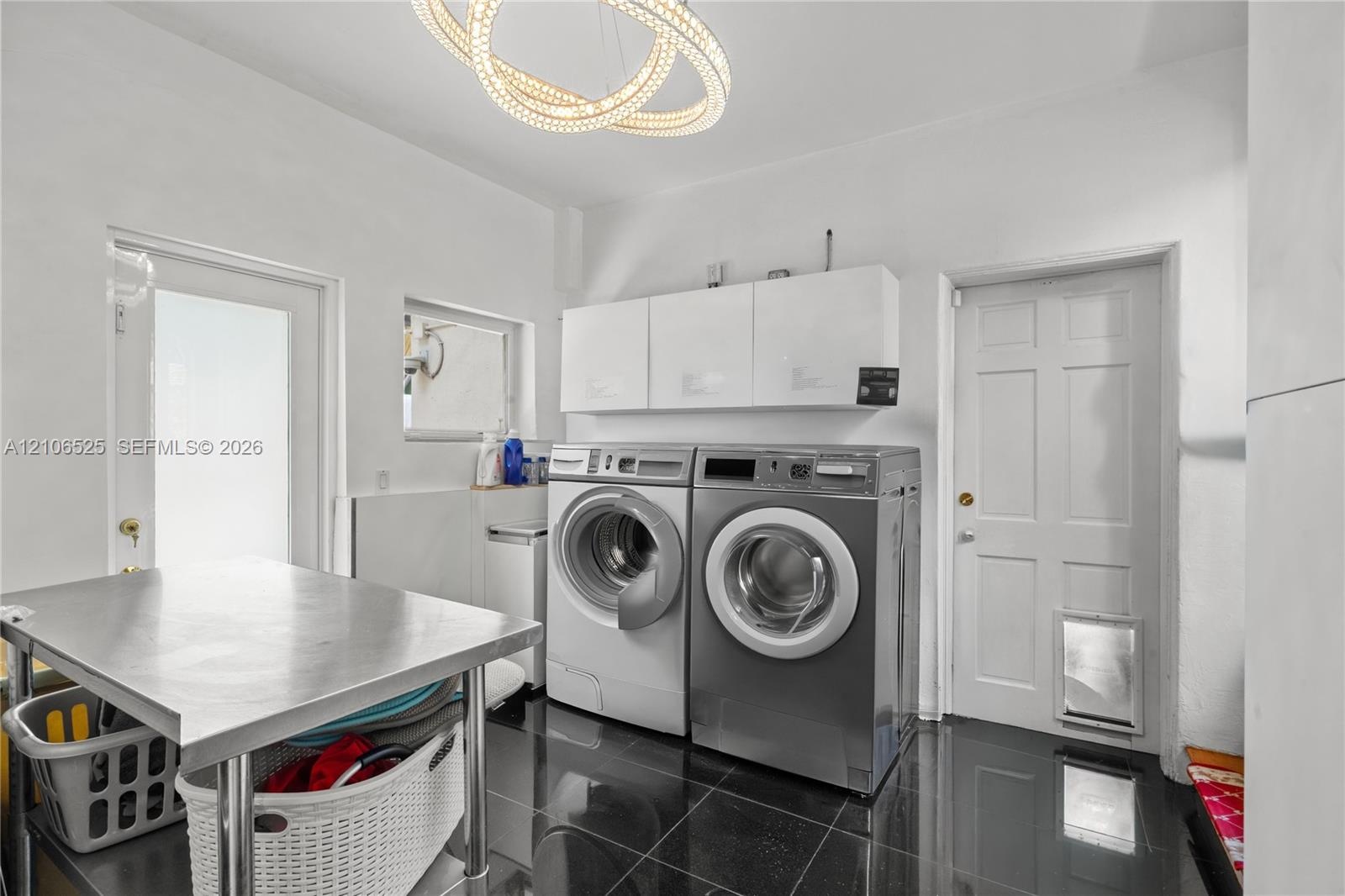 Utility room featuring polished dark tile flooring, white wall-mounted storage cabinetry, a contemporary circular dual-ring chandelier, and a six-pane
