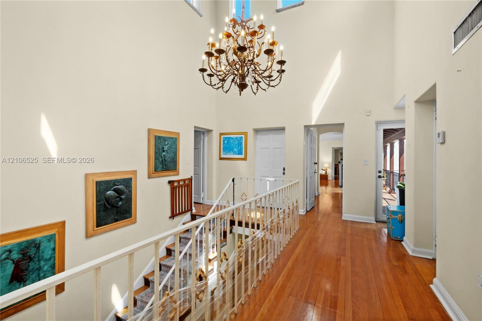 Vaulted ceiling featuring a multi-tiered crystal chandelier, wood-finish flooring, and a decorative metal railing
