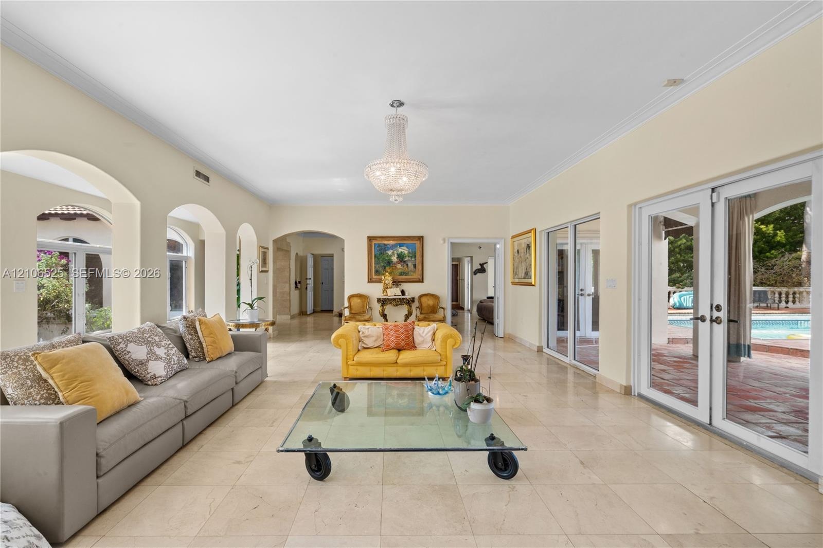 Spacious living area featuring polished stone flooring, arched architectural details, a central crystal chandelier, and two sets of glass-paned double