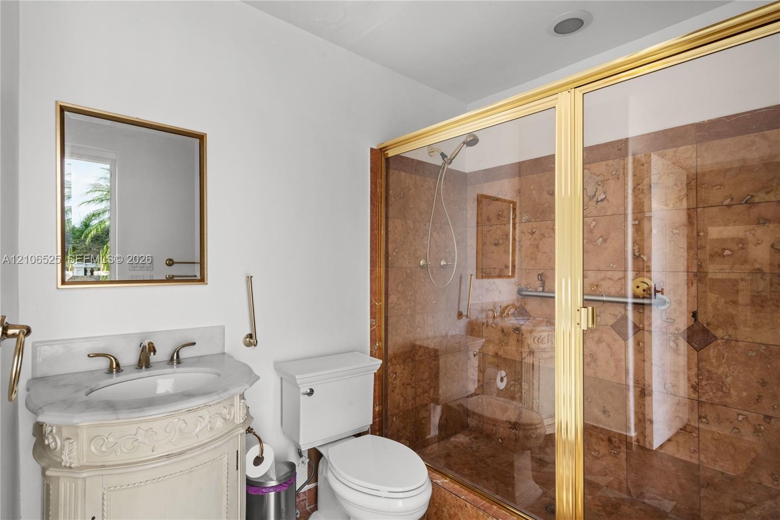 Bathroom featuring a stone-topped vanity with ornate carved base, wall-mounted mirror with gold-finish frame, and walk-in shower with floor-to-ceiling