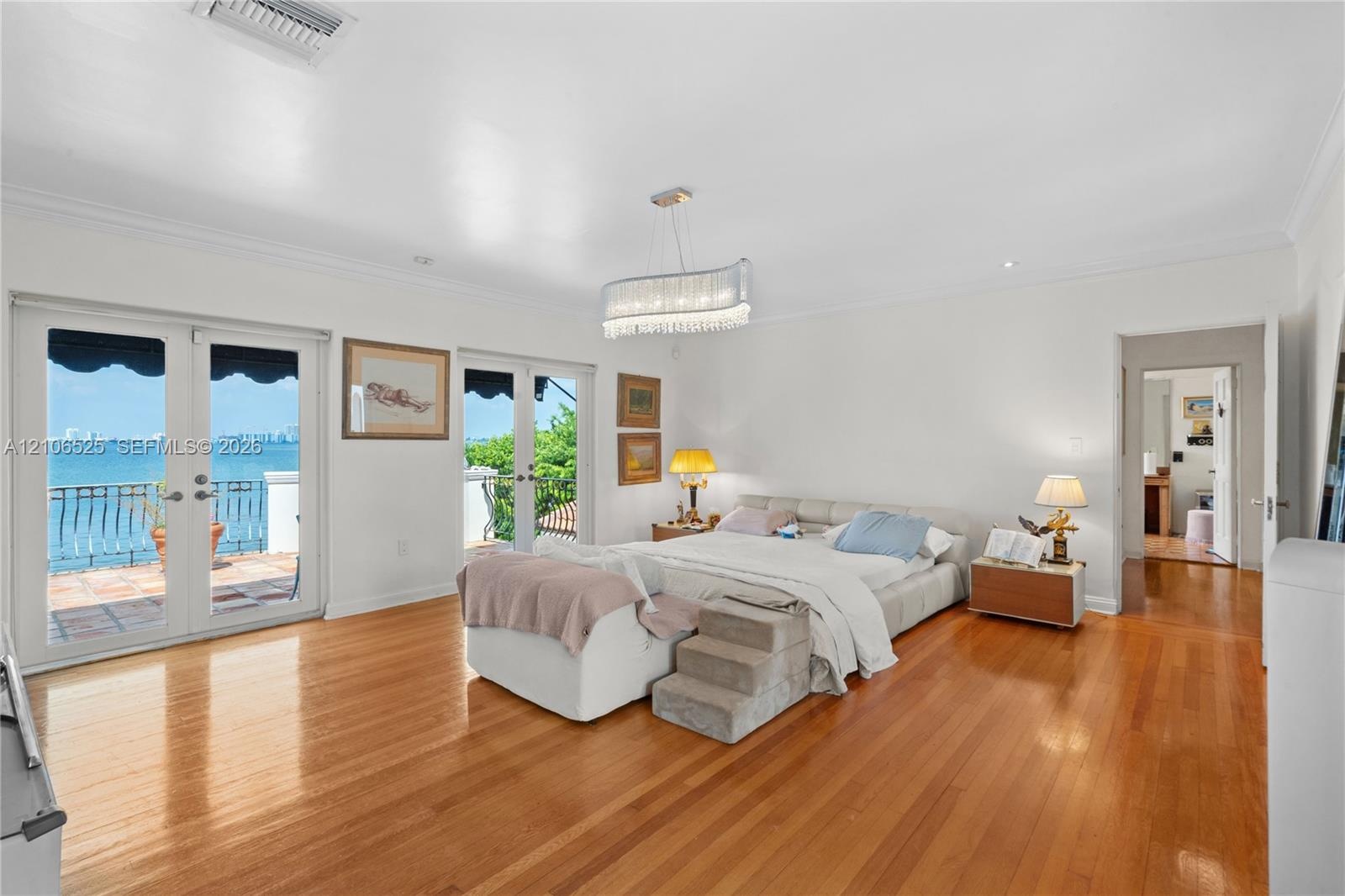 Spacious interior featuring wood-finish flooring, dual sets of French doors, crown molding, a decorative crystal chandelier, and a balcony with water 