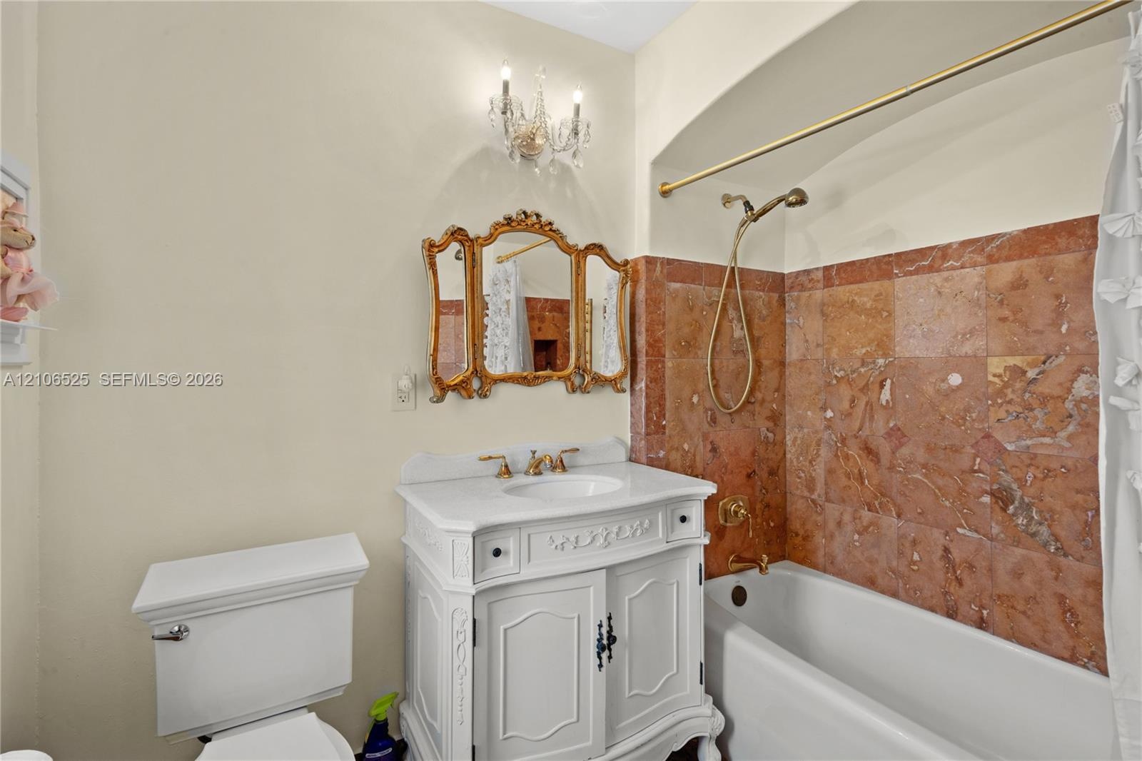 Bathroom featuring a white vanity with carved detailing, stone tile shower surround, brass-finish fixtures, gold-toned ornamental mirror, and a crysta