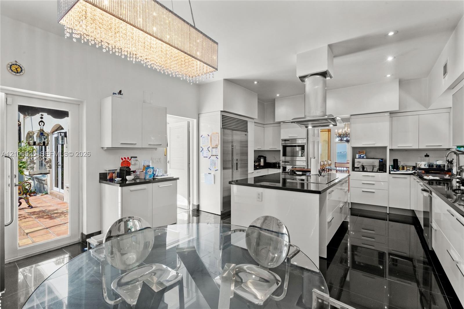Gourmet kitchen featuring high-gloss cabinetry, a central island with a stone countertop, stainless steel appliances, a cylindrical range hood, and a 