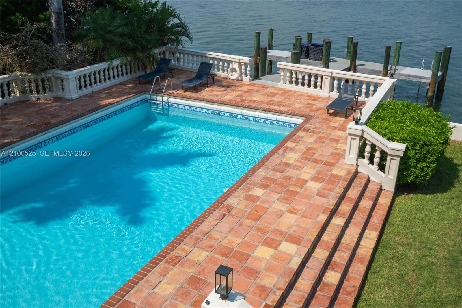 In-ground swimming pool featuring a terra-cotta tile deck, a balustrade perimeter railing, and a private wooden dock extending over the water