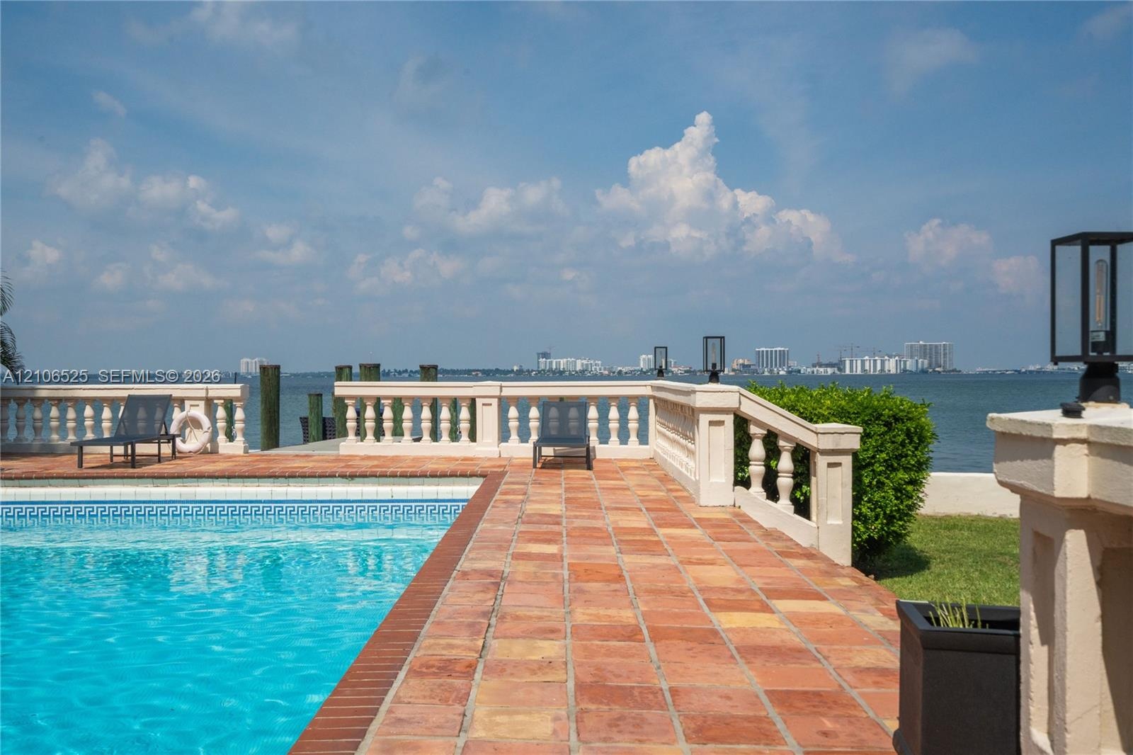 In-ground swimming pool with tile border, terracotta tile patio, and concrete balustrade railing overlooking the water