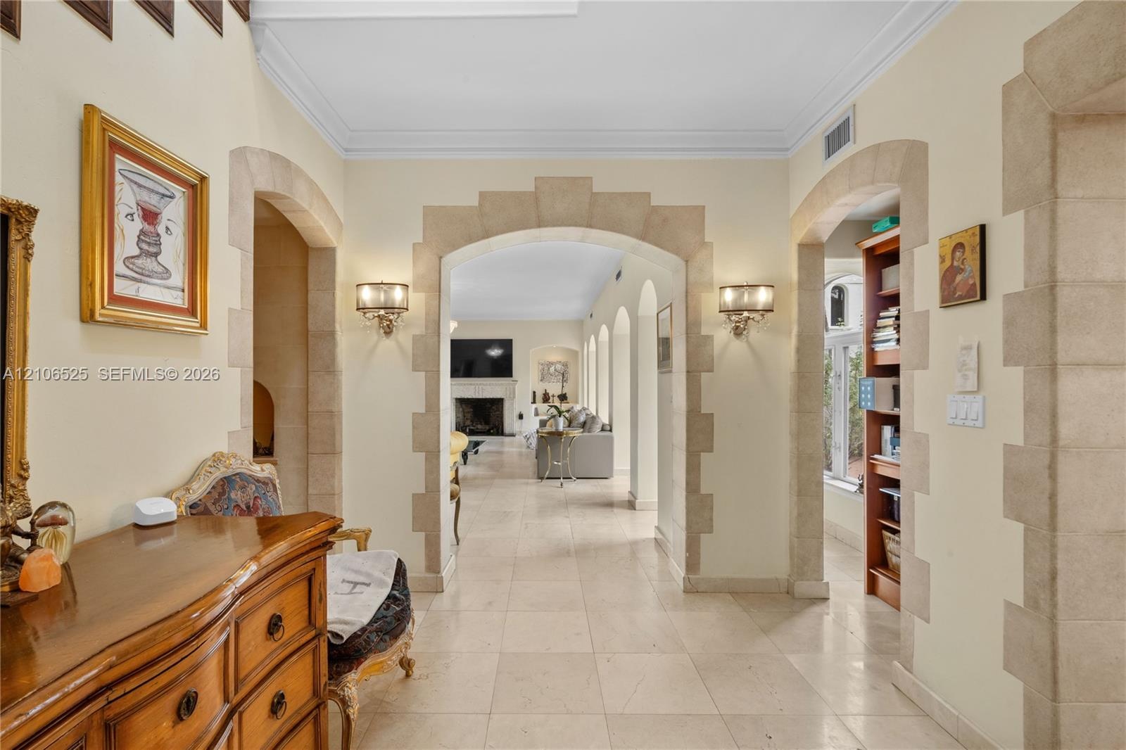 Foyer featuring arched stone-trimmed doorways, crown molding, stone tile flooring, and wall-mounted light fixtures