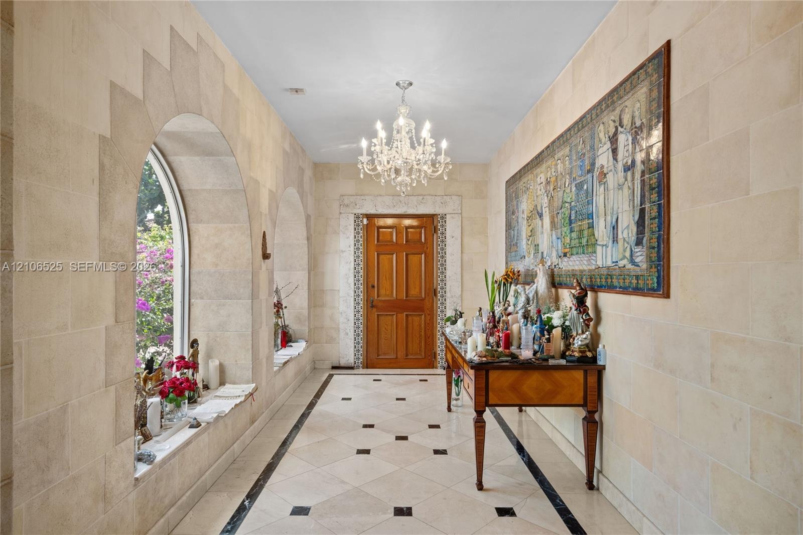 Entryway featuring natural stone block walls, arched window alcoves, tile flooring with decorative stone insets, a crystal chandelier, and a solid woo