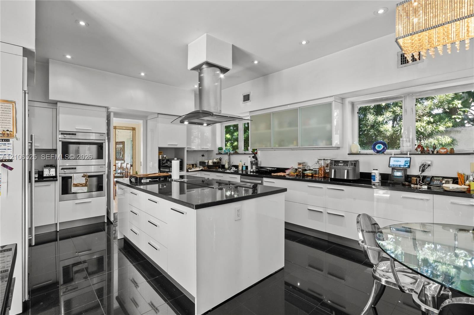 Modern kitchen featuring high-gloss cabinetry, a central island with a stone-finish countertop, stainless steel double wall ovens, a ceiling-mounted s