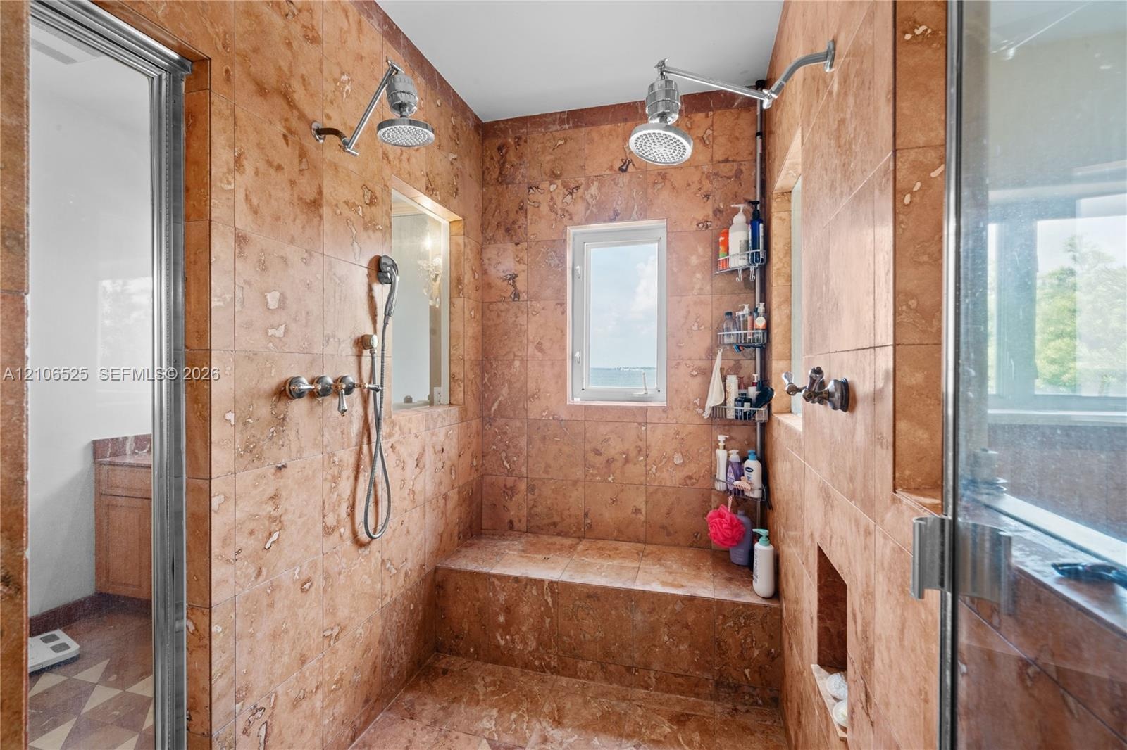 Walk-in shower enclosure featuring floor-to-ceiling stone tile, a built-in tiled bench, dual overhead rainfall showerheads, a handheld shower fixture,