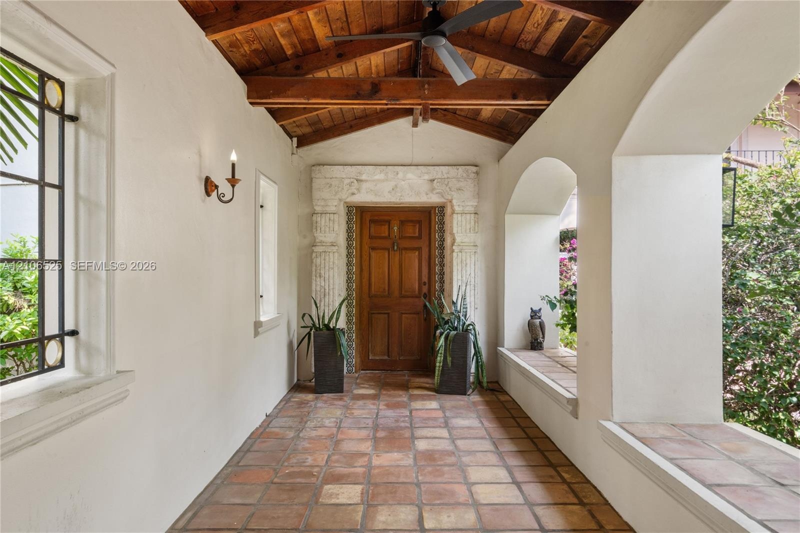 Covered entryway featuring terracotta tile flooring, exposed wood-beam vaulted ceiling, arched masonry openings, stone door surround with column detai