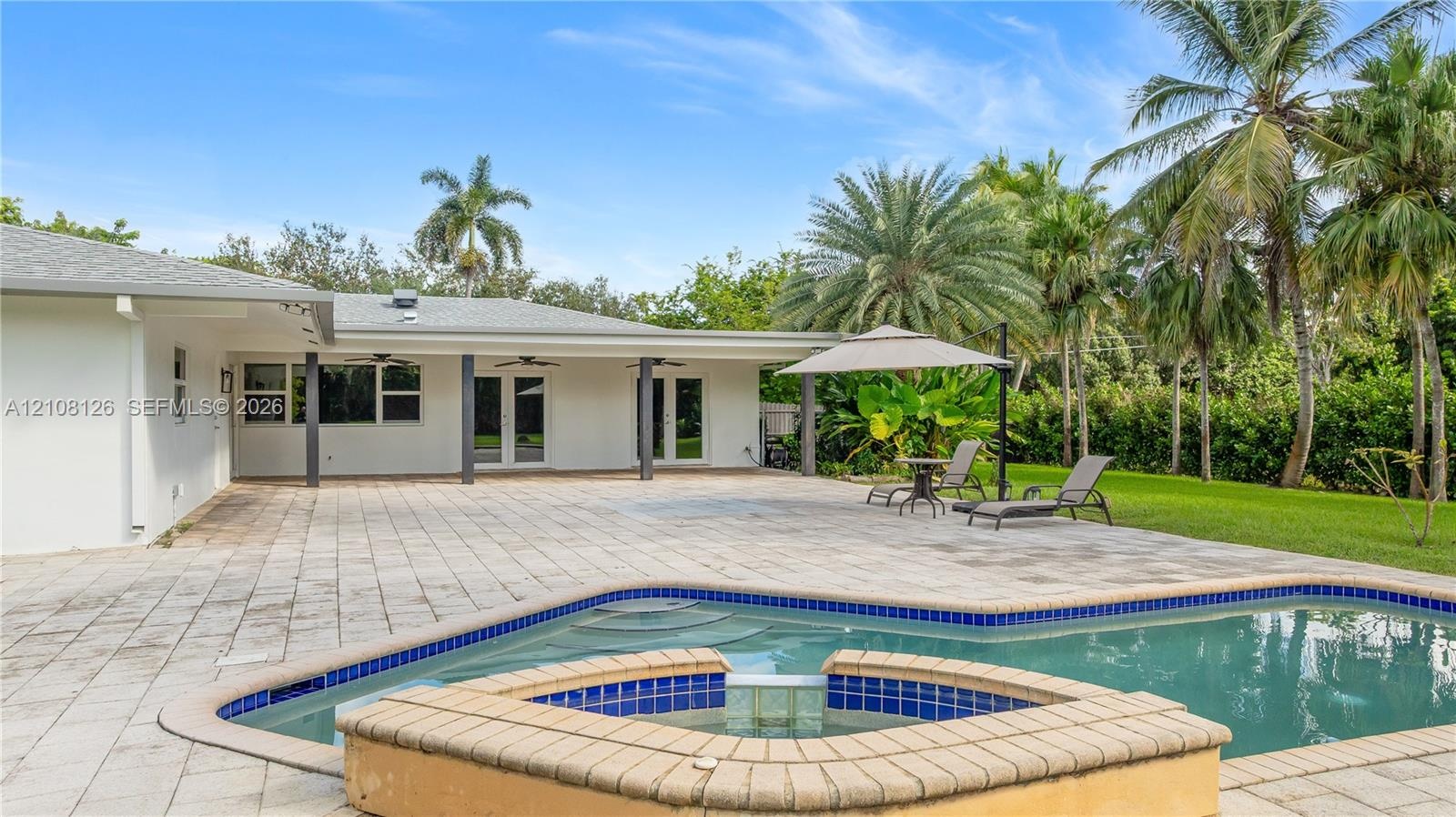 Backyard featuring a paved stone patio, an in-ground swimming pool, a raised tile-accented spa, and a covered lanai