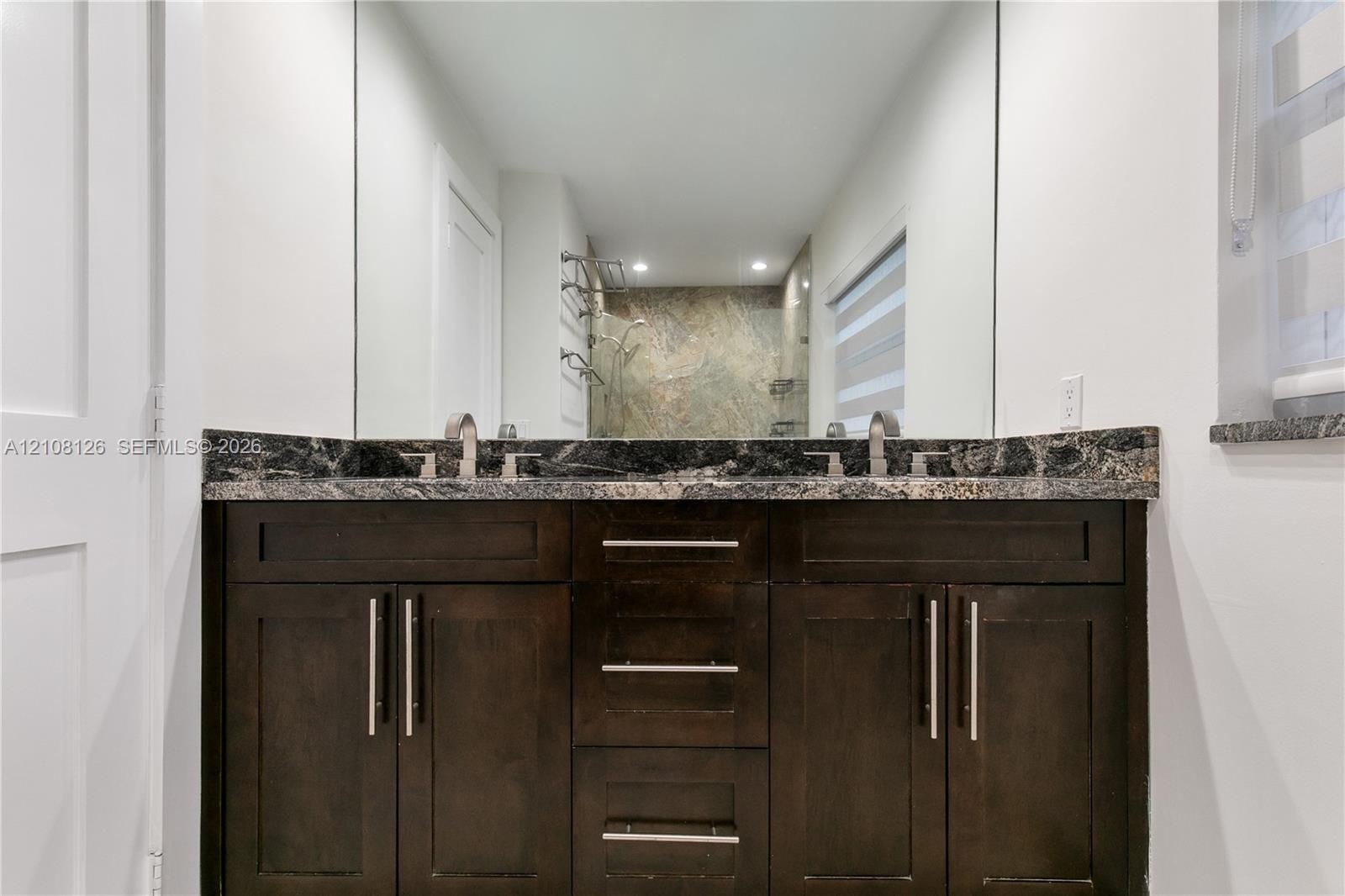 Dark-stained wood cabinetry featuring brushed nickel hardware, expansive vanity mirror, stone countertop, and dual under-mount sinks