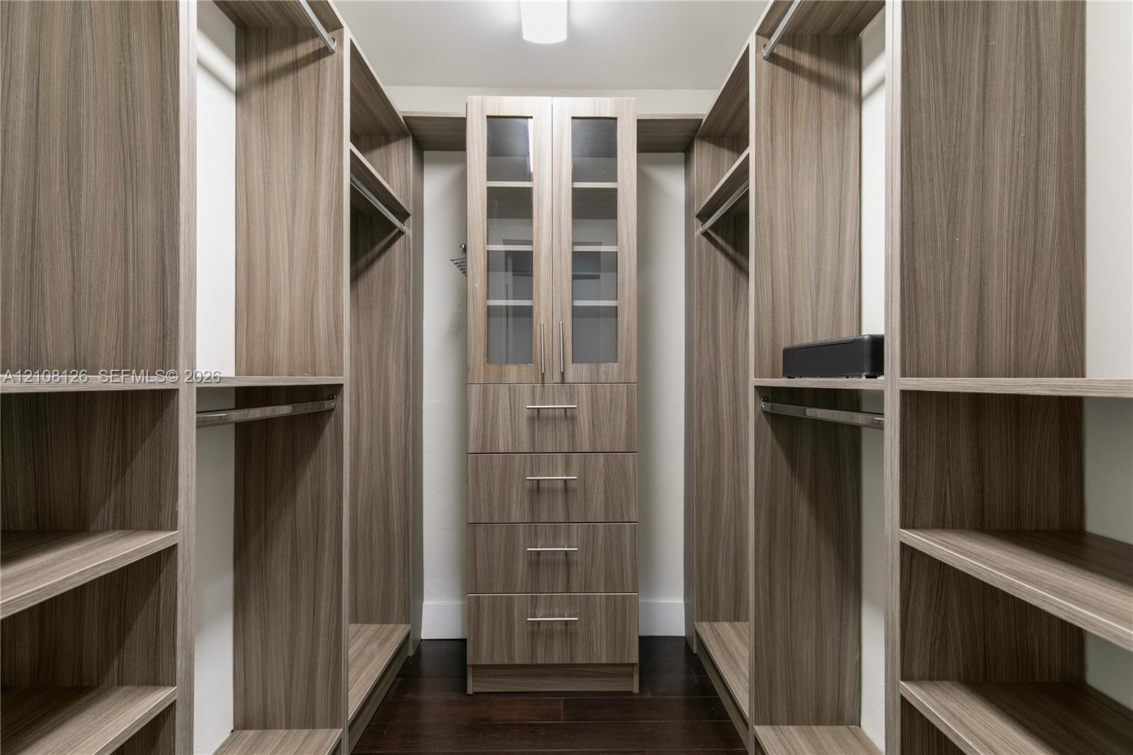 Custom walk-in closet featuring extensive wood-finish shelving, integrated hanging rods, a central stack of four soft-close drawers, and upper cabinet