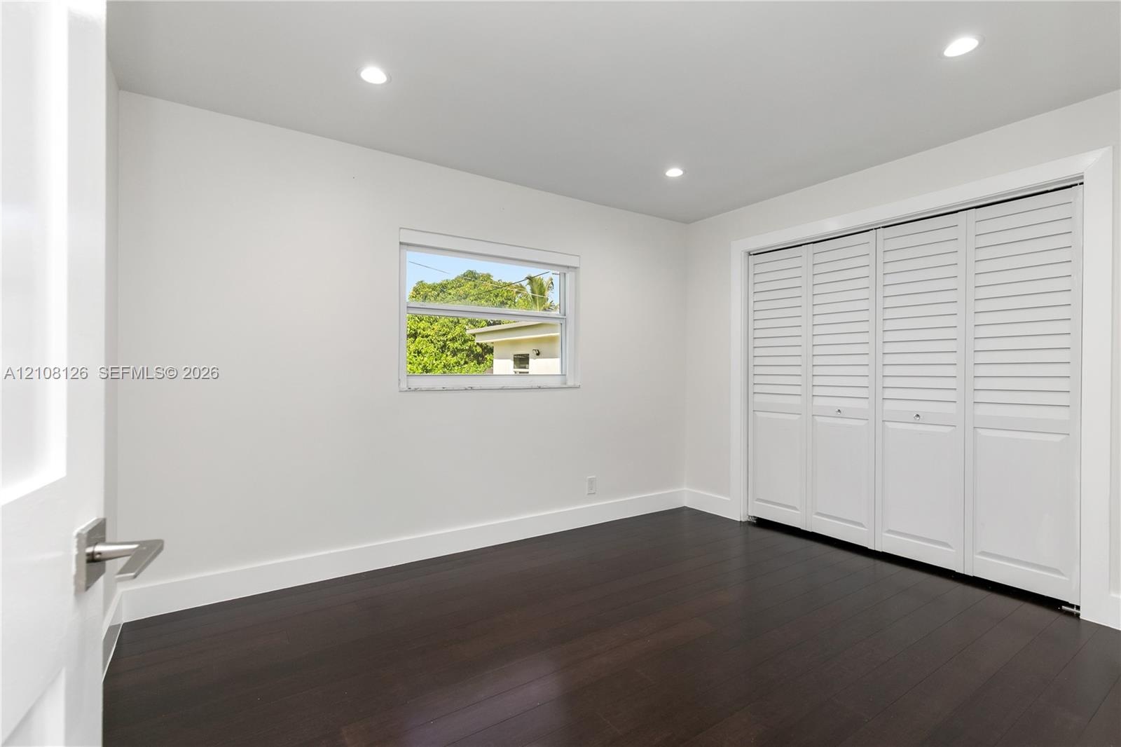 Room featuring dark wood-finish flooring, recessed lighting, and a large bi-fold closet with white louvered panels