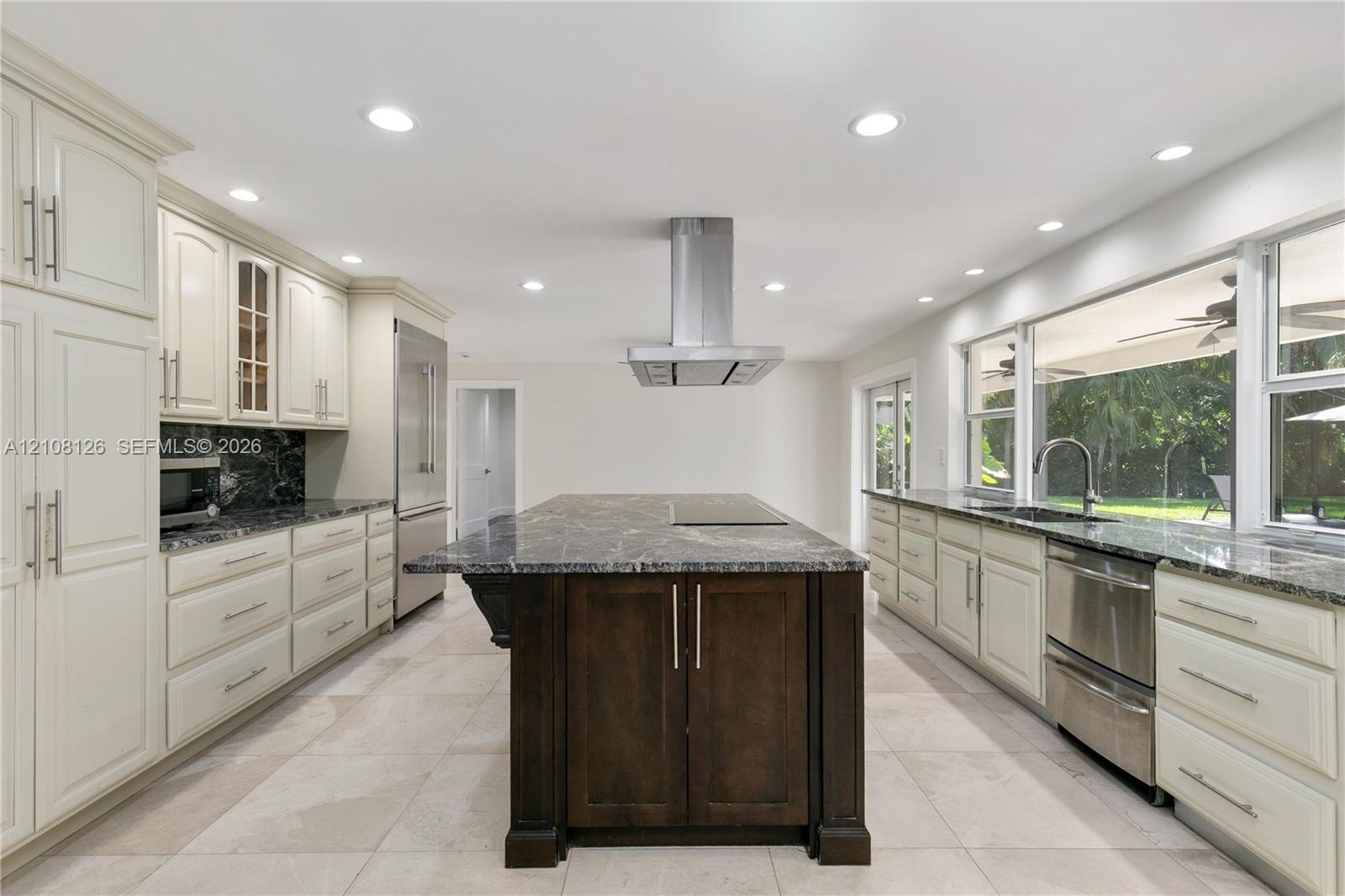 Kitchen featuring light-toned cabinetry, a dark-toned center island with a built-in cooktop, stainless steel range hood, stone-finish countertops, and