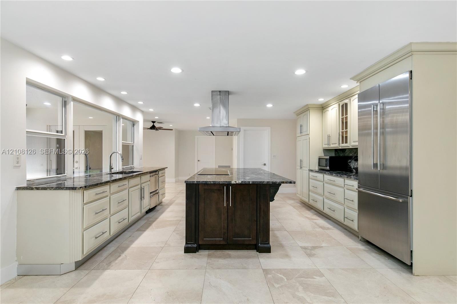 Kitchen featuring a central island with a stone countertop, custom cabinetry, stainless steel refrigerator, stone-tiled flooring, and recessed ceiling