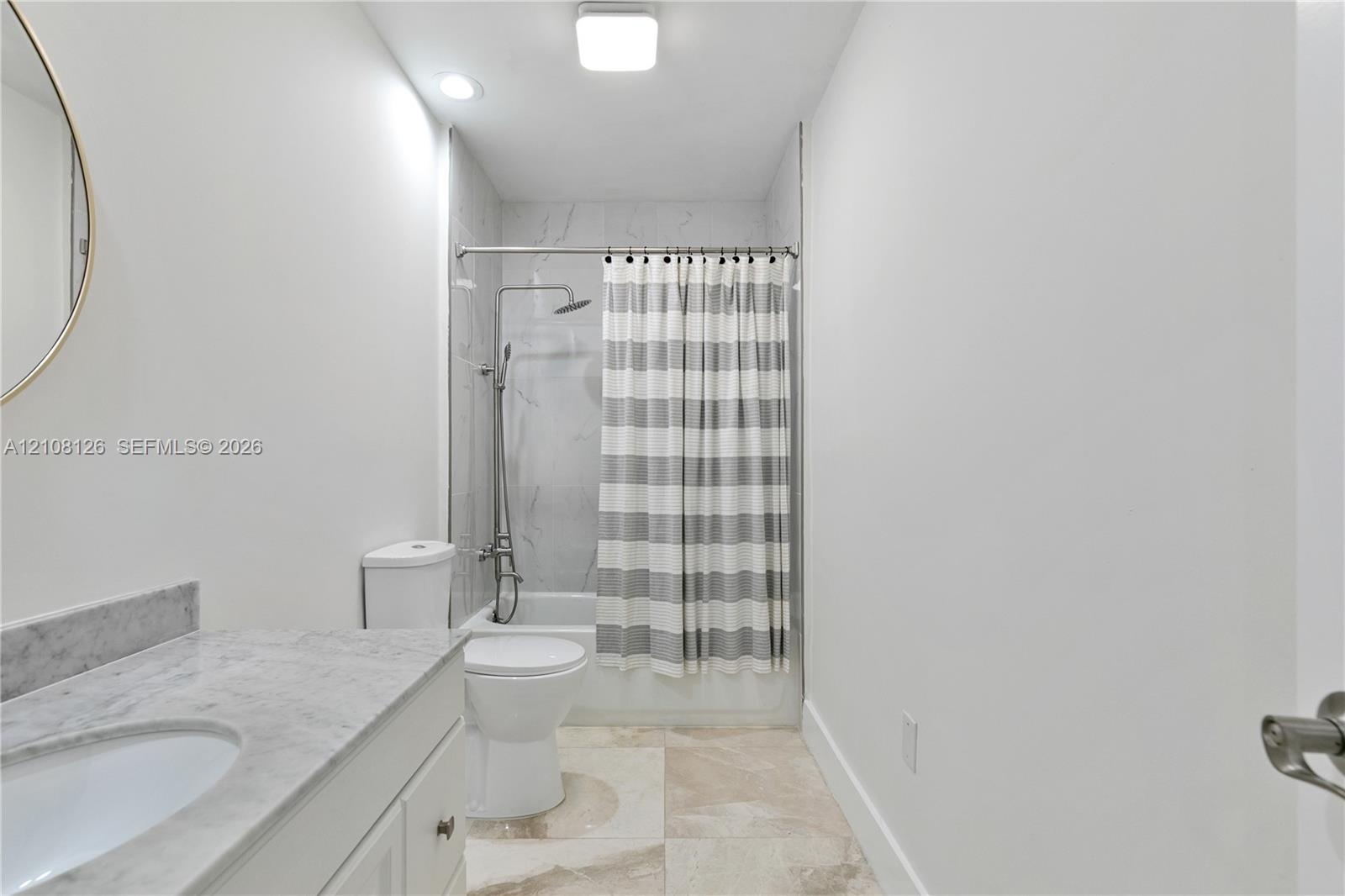 Bathroom featuring a vanity with a stone-top counter, undermount sink, shower-tub combination with stone-style surround, and tile flooring