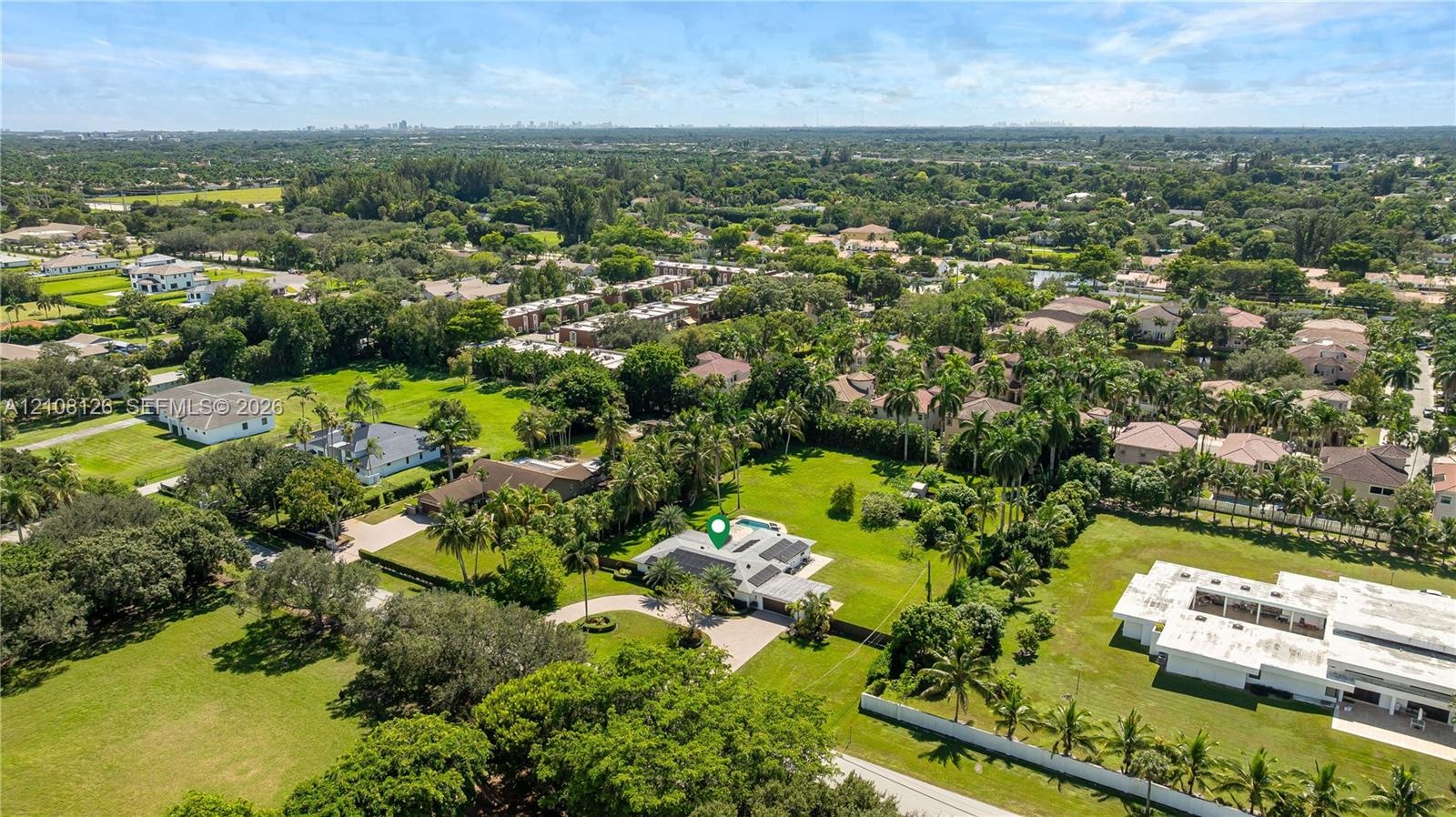 Aerial perspective of a sprawling property featuring a circular driveway, expansive manicured grounds, mature palm trees, and an in-ground swimming po