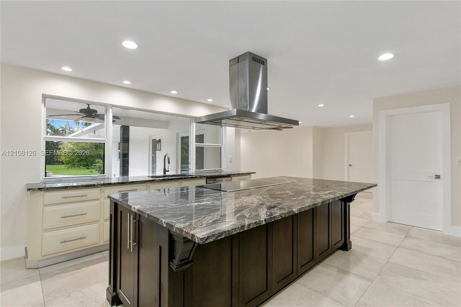Kitchen featuring a large central island with dark cabinetry and stone-finish countertop, stainless steel ceiling-mounted range hood, light-colored pe