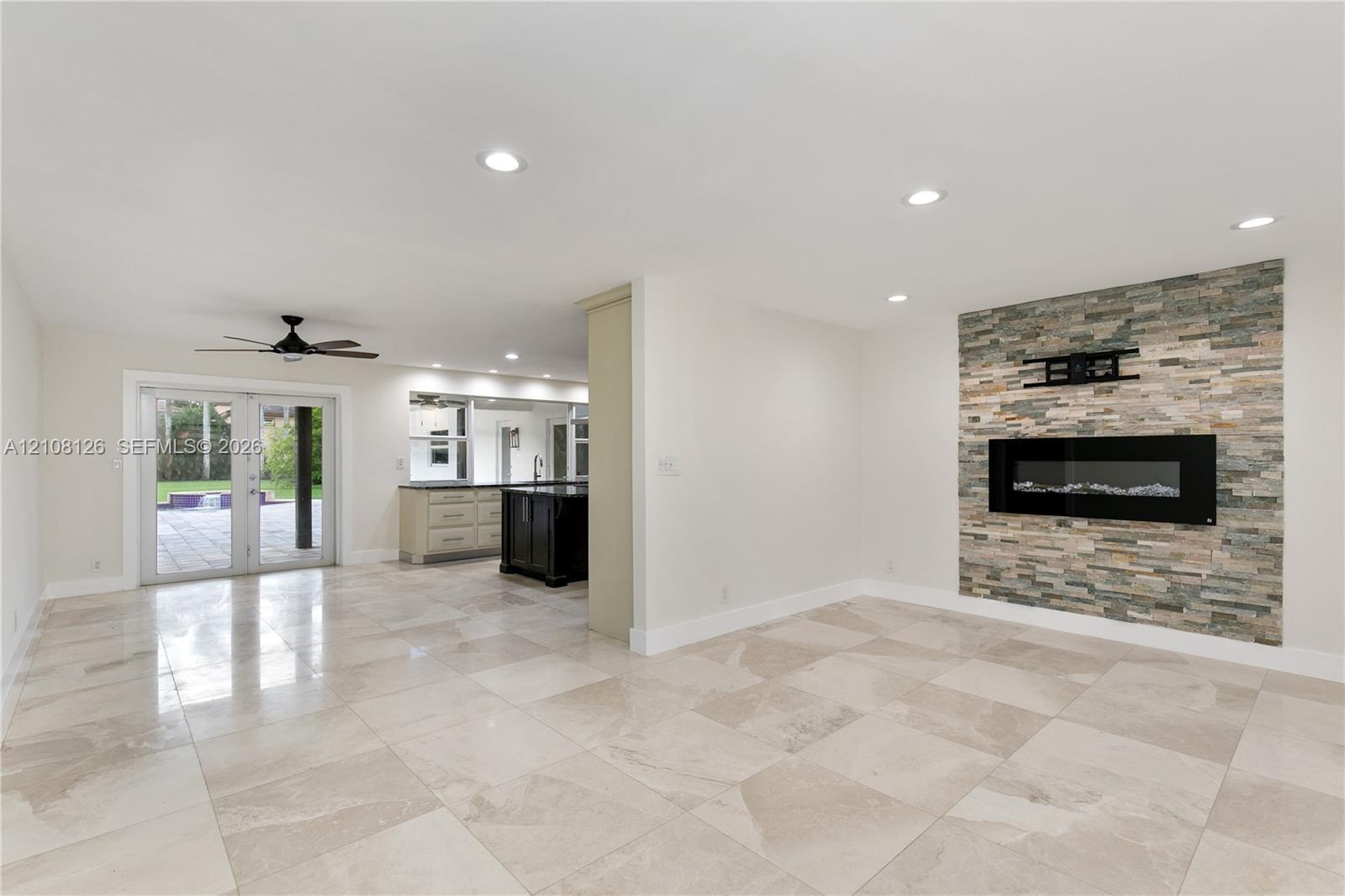 Living area featuring large-format tile flooring, recessed lighting, and a floor-to-ceiling stone-veneer accent wall with an integrated electric firep