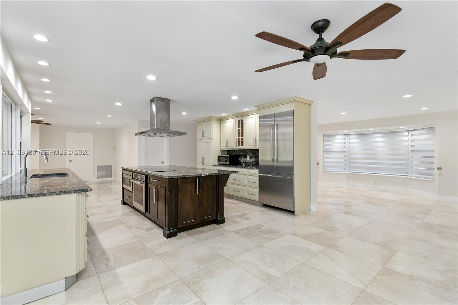 Kitchen featuring a center island with dark wood-finish cabinetry, stainless steel appliances, a stainless steel range hood, stone countertops, and ti