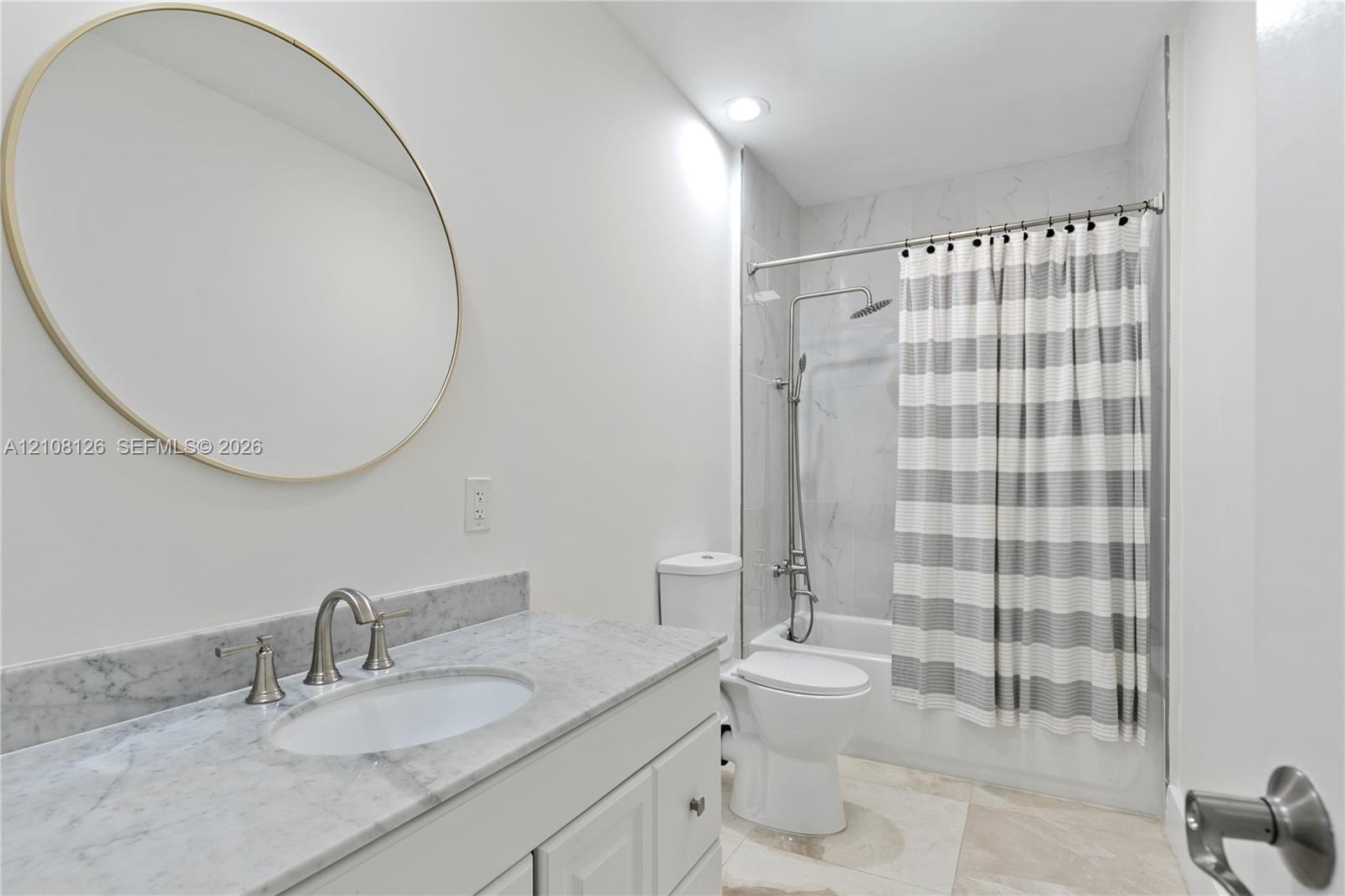 Bathroom featuring a vanity with natural stone countertop, undermount sink, circular wall mirror, and a tub-shower combination with floor-to-ceiling t