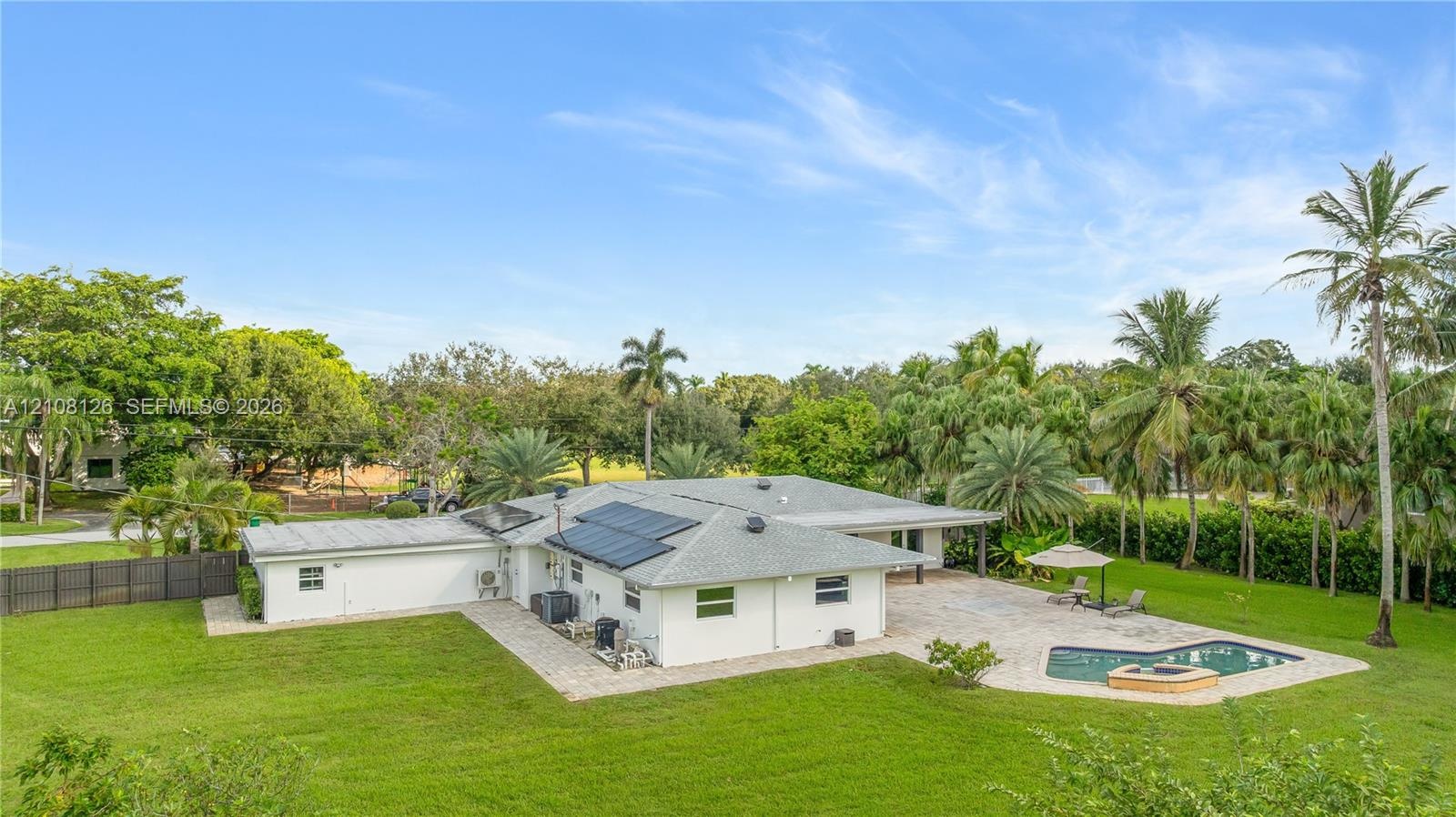 Expansive backyard featuring a paver patio, in-ground pool with a spillover spa, solar panel array, and mature landscaping