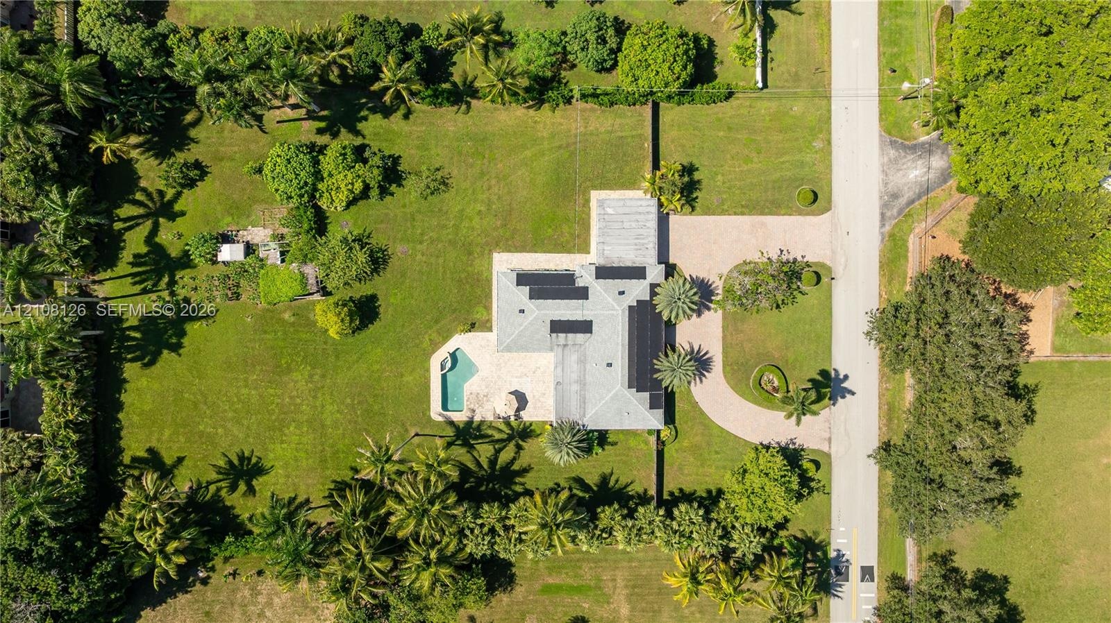 Aerial perspective featuring an expansive lot, a private swimming pool, solar panels, and a paved circular driveway