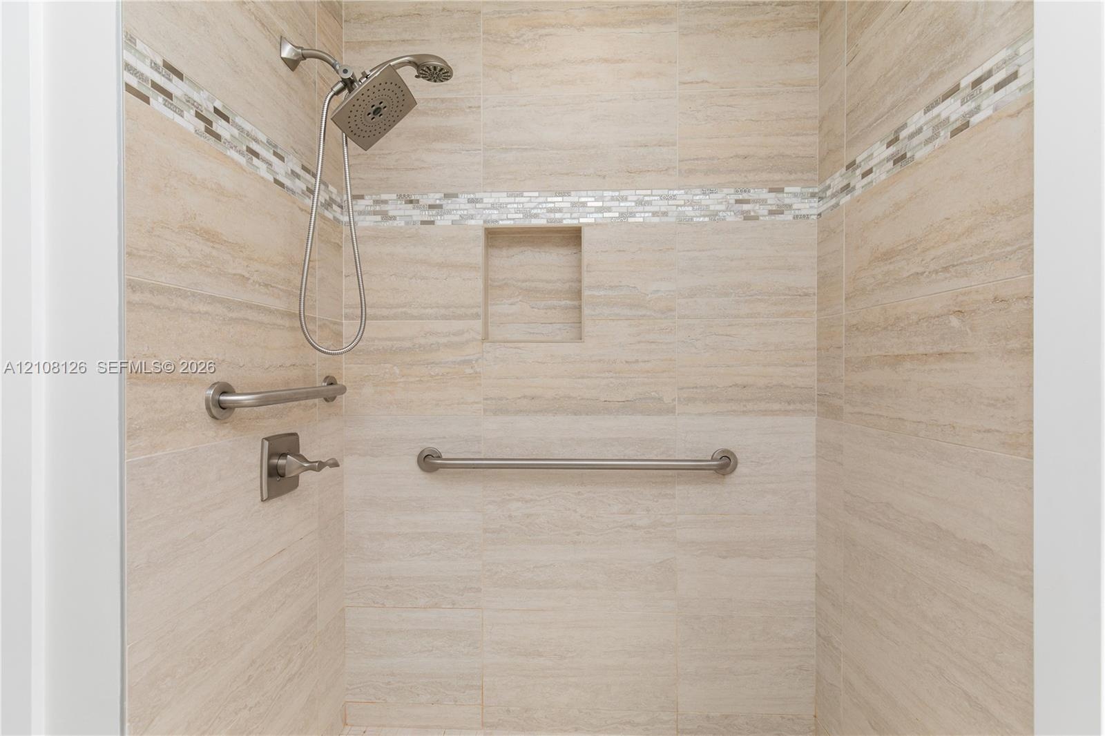 Walk-in shower featuring neutral stone-finish tile surround, integrated mosaic accent banding, built-in recessed niche, handheld shower fixture, and b