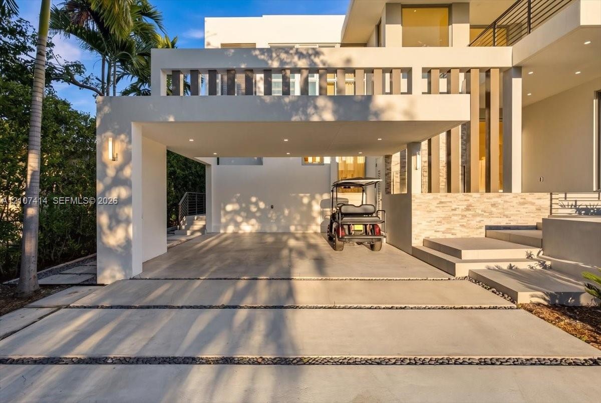 Modern architectural facade featuring a covered porte-cochère, recessed lighting, stacked stone exterior detailing, and a concrete driveway with decor
