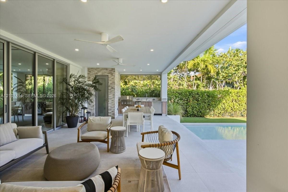 Covered outdoor patio featuring light-toned tile flooring, recessed ceiling lighting, ceiling fans, and a built-in outdoor kitchen with an integrated 