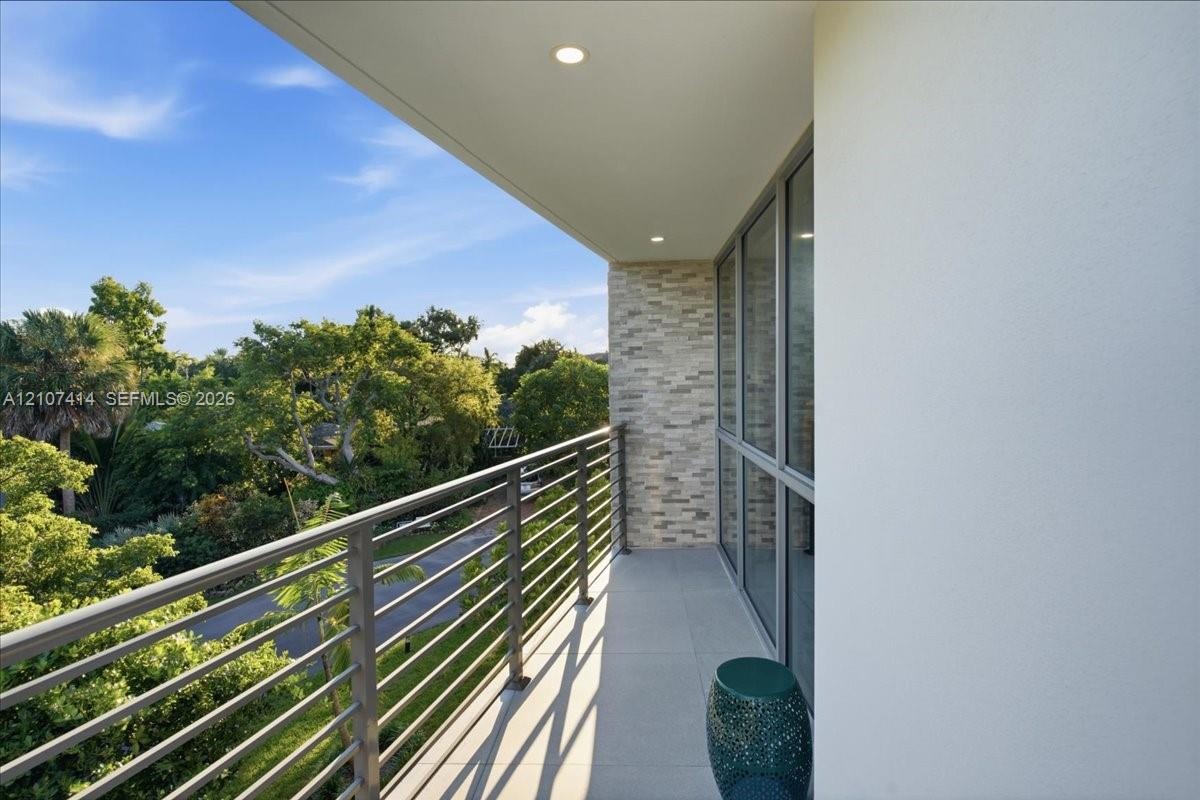 Covered balcony featuring horizontal metal railings, large-format tile flooring, recessed ceiling lighting, and a textured stone wall finish
