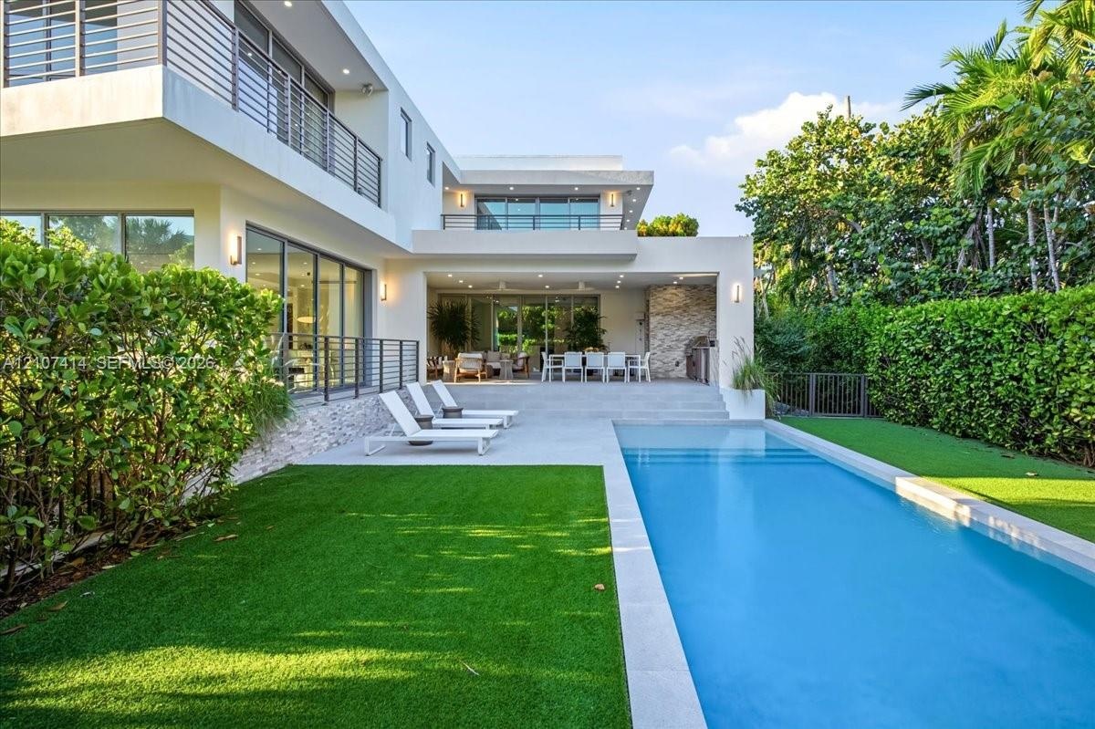 Contemporary multi-level exterior featuring stucco facade, rectangular swimming pool, concrete patio, second-story balconies with horizontal railings,